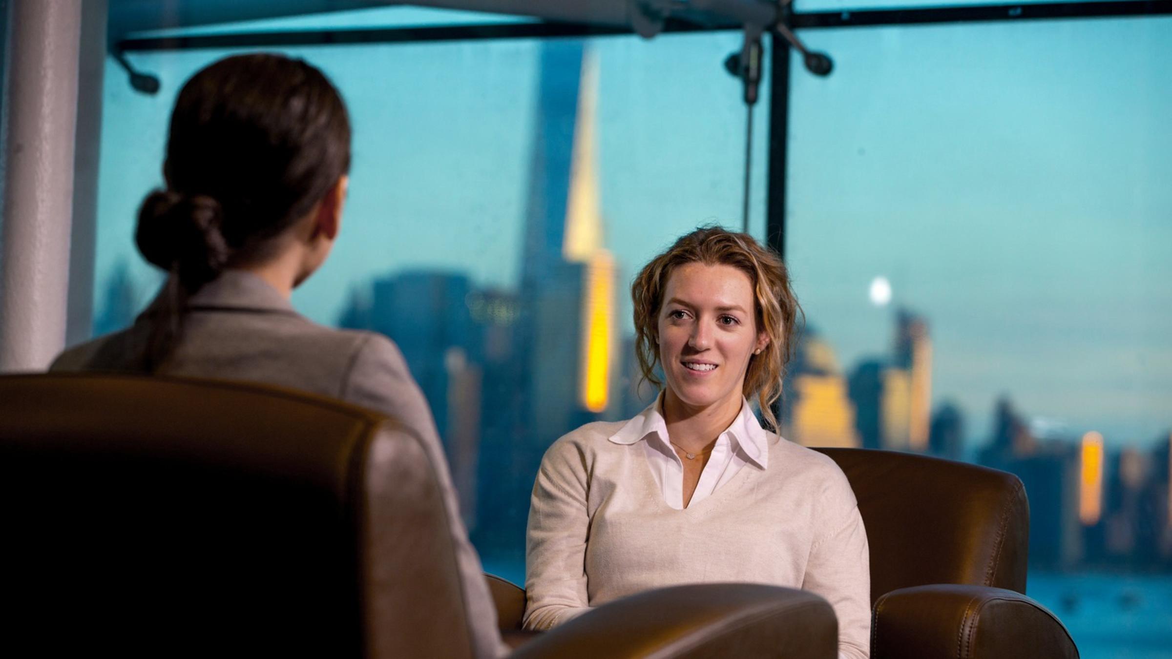 Two women talking while sitting in chairs with NYC skyline in background