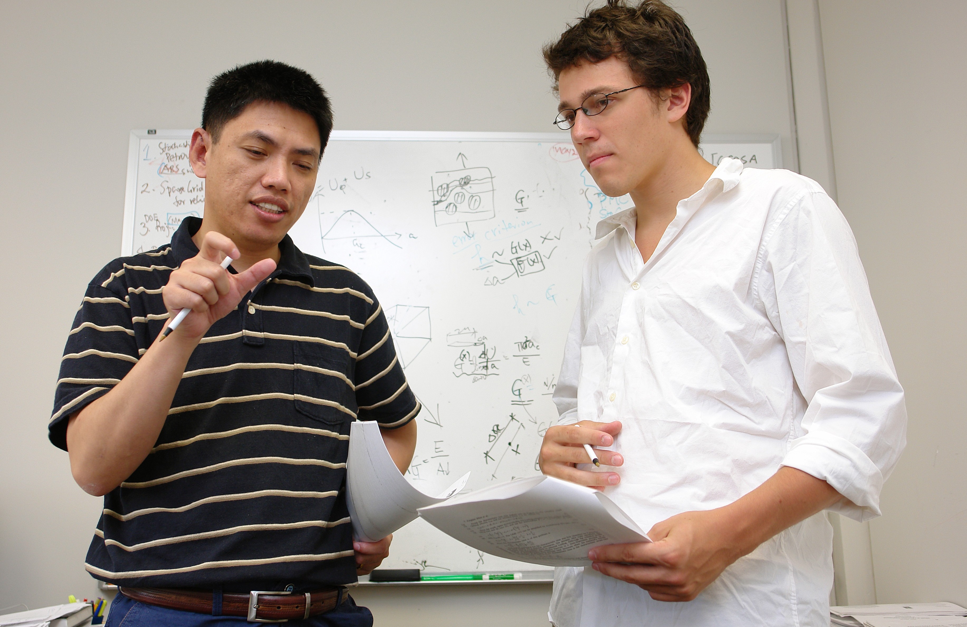 A male faculty talking to a male student in a classroom with a whiteboard in the background
