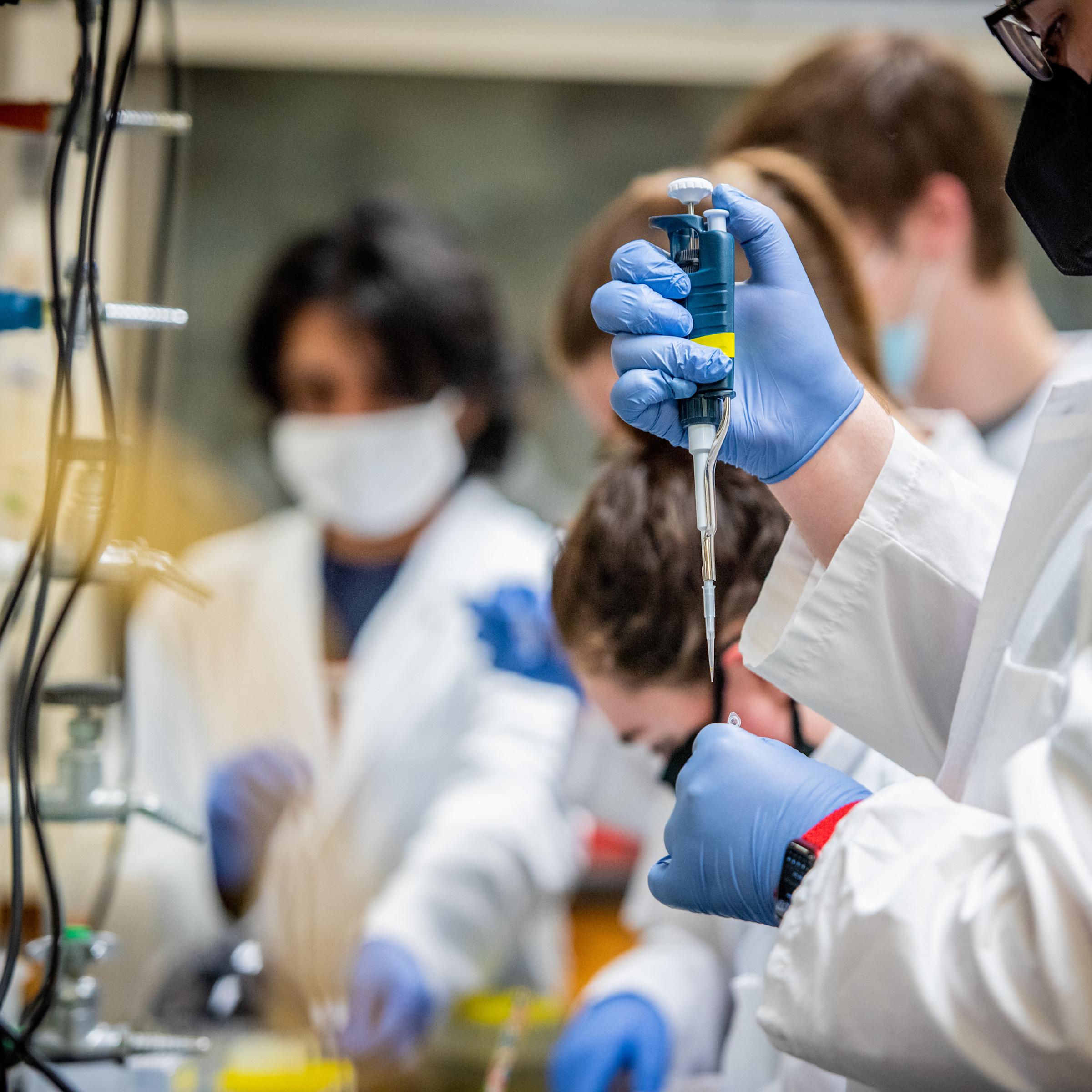 Male and female students working in a lab with a syringe.