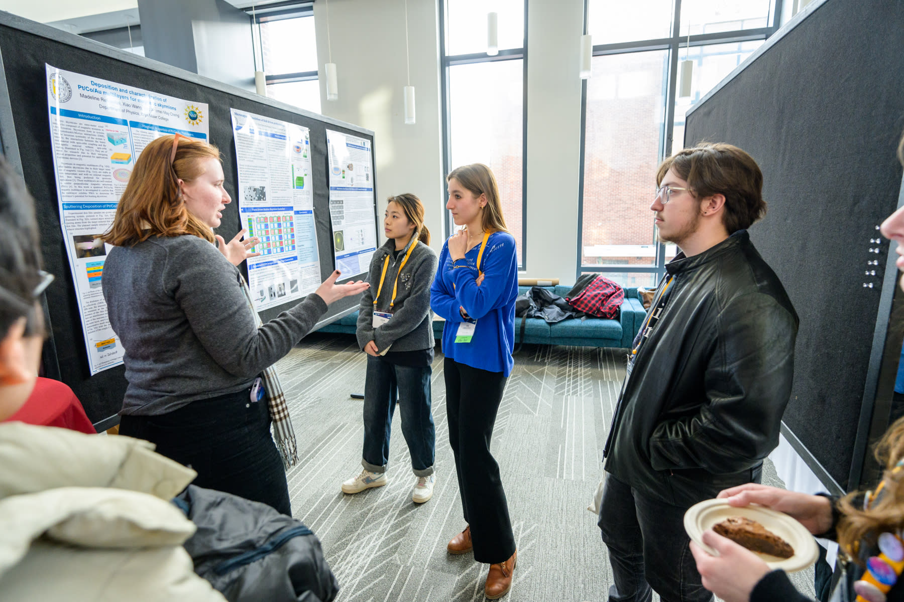 A group of students discuss a poster presentation in an exhibition hall.