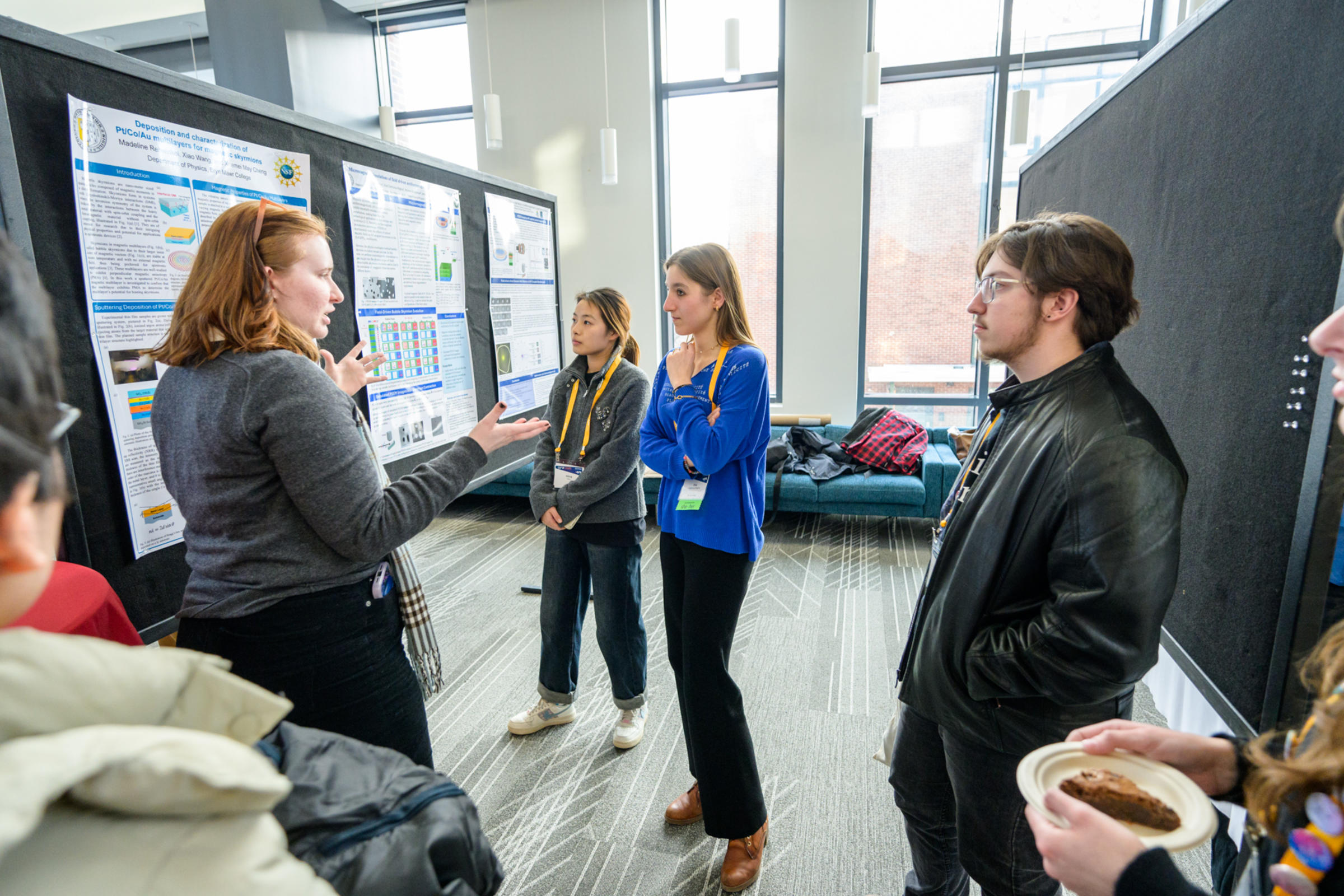 A group of students discuss a poster presentation in an exhibition hall.