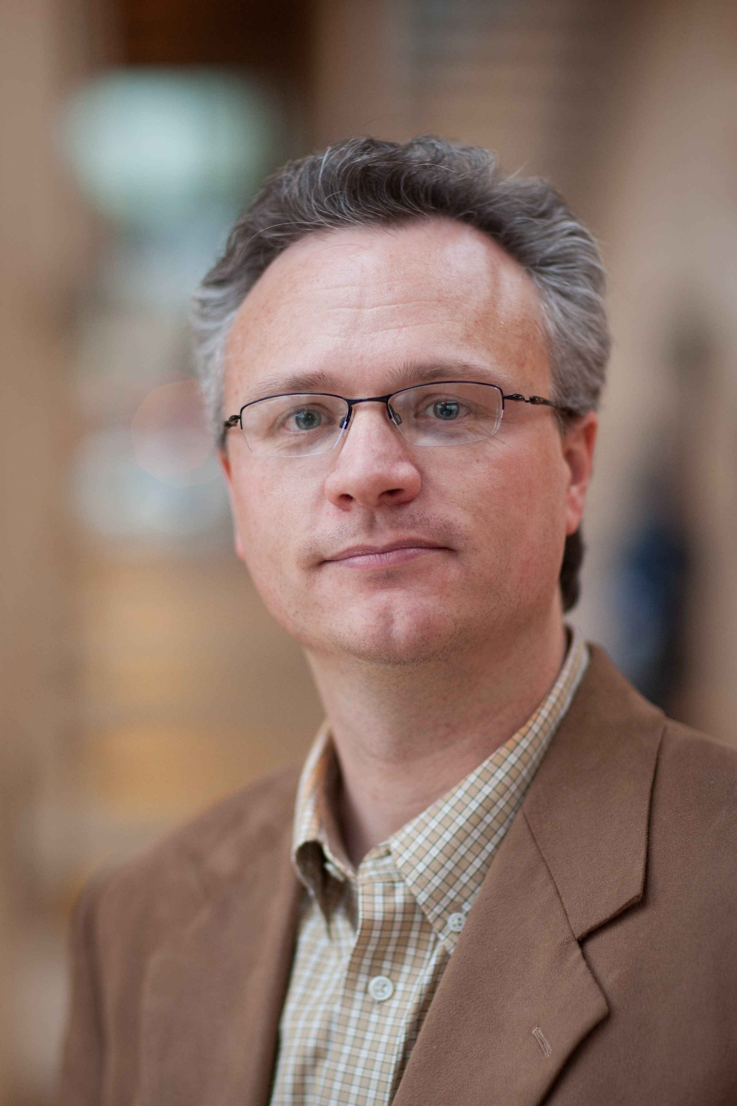Michael Barnett head and shoulders photo wearing a tan blazer with a light tan and white checkered shirt.