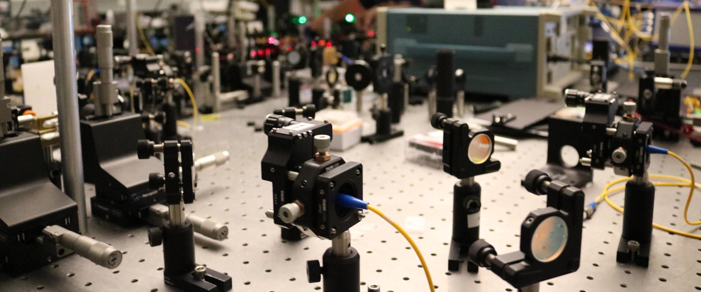 A photo of a male student working in the quantum lab surrounded by wires and photonics equipment.
