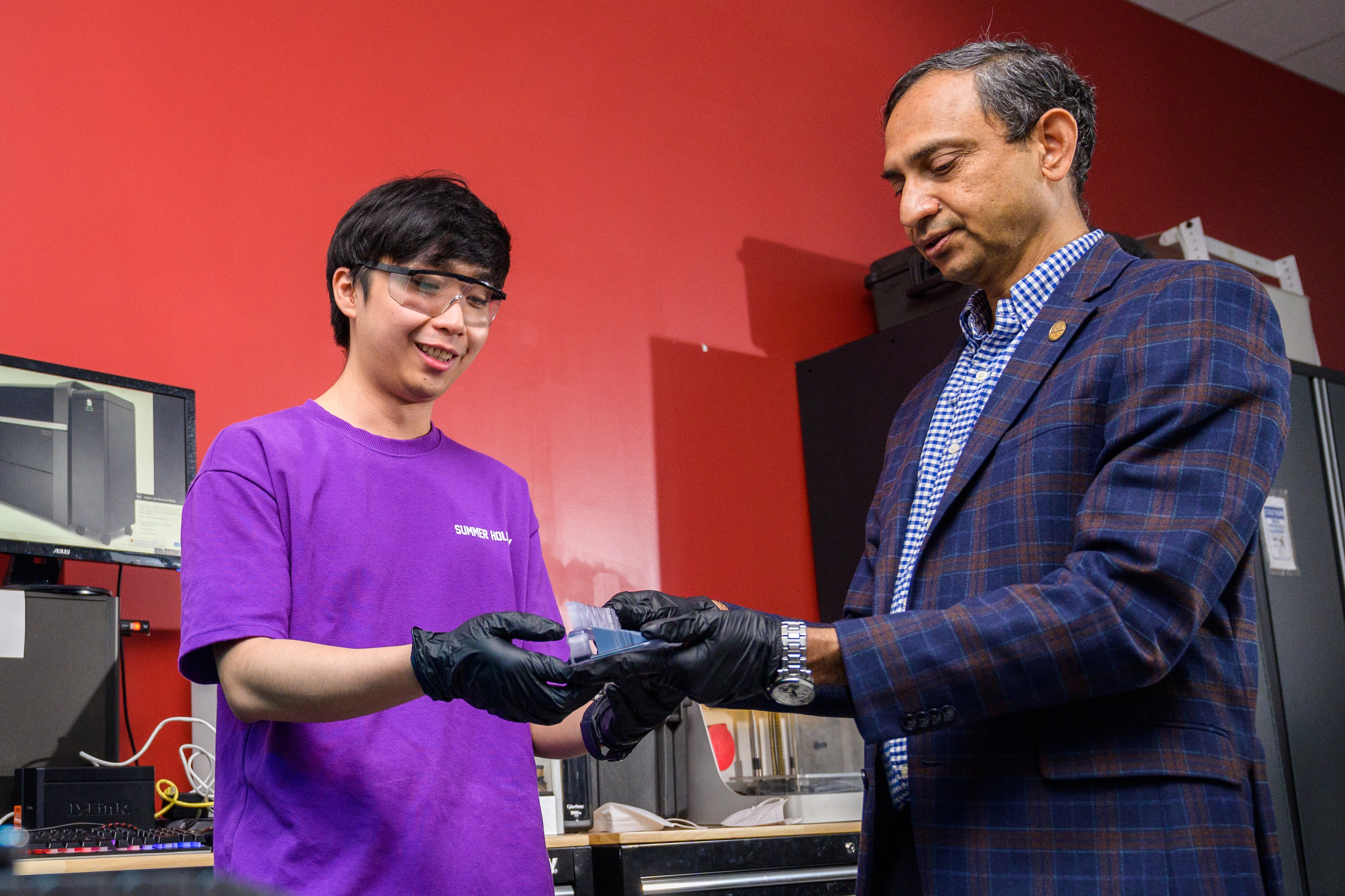 Stevens professore Kishore Pochiraju examines an item in a lab next to a Stevens student in a purple shirt.