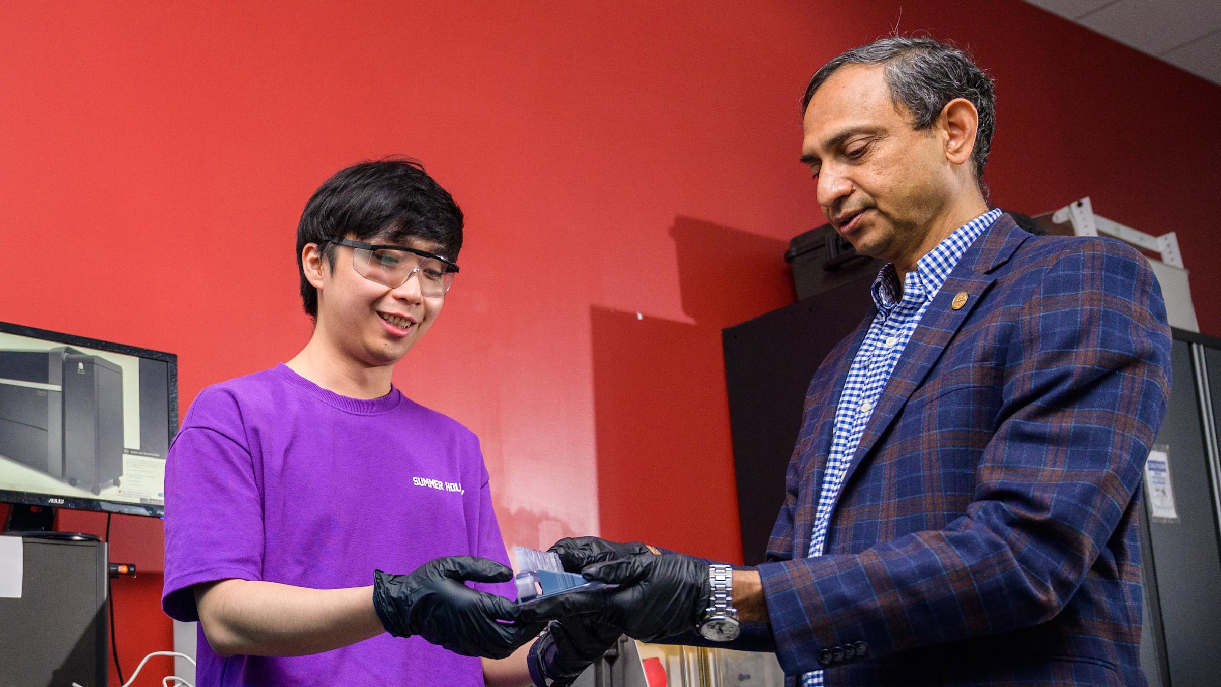 Stevens professore Kishore Pochiraju examines an item in a lab next to a Stevens student in a purple shirt.