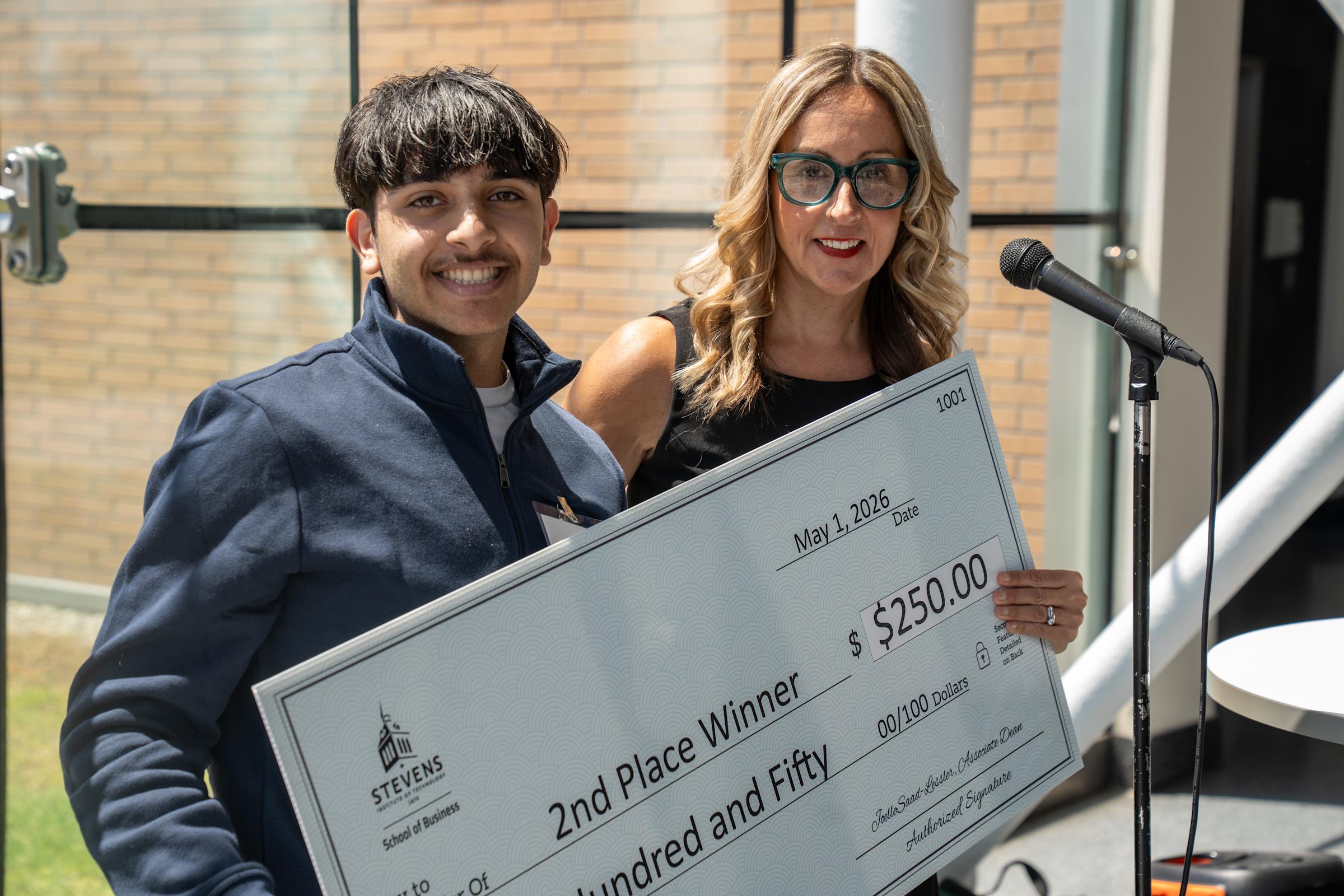 Image 2: A smiling male student in a navy quarter-zip poses with a woman in black and teal glasses holding a large ceremonial check for $250 made out to "2nd Place Winner" from Stevens School of Business, dated May 1, 2026, for Stevens Trading Day 2026.