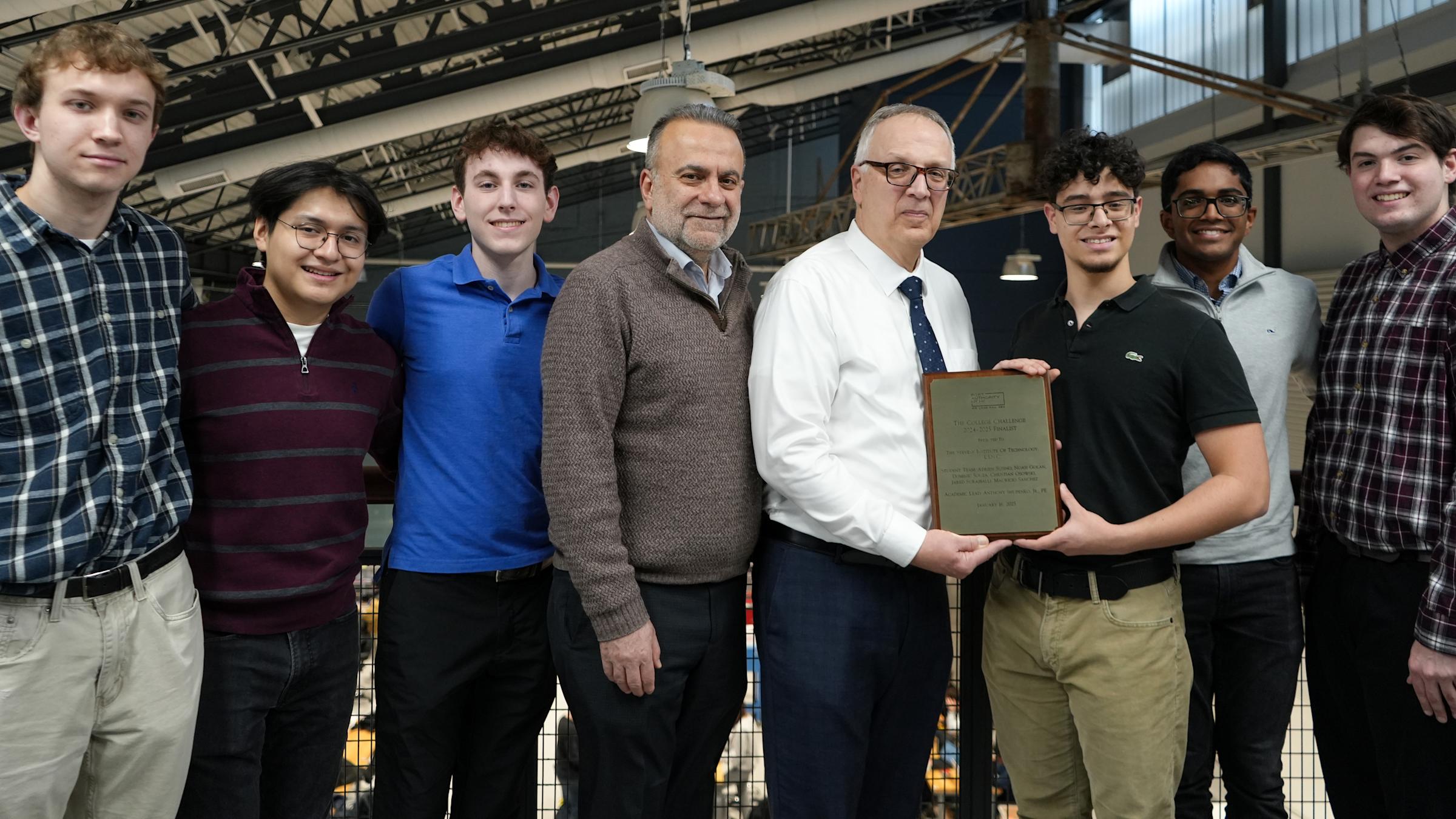 Two professors stand in the middle of a line with three students one each side posing with a plaque.