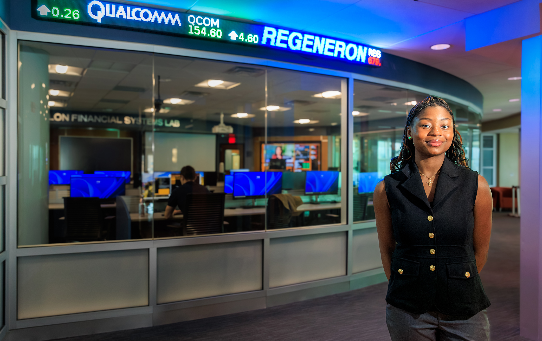 Victoria Okonkwo stands to the right of the stock exchange ticker outside the Hanlon Financial Systems Center