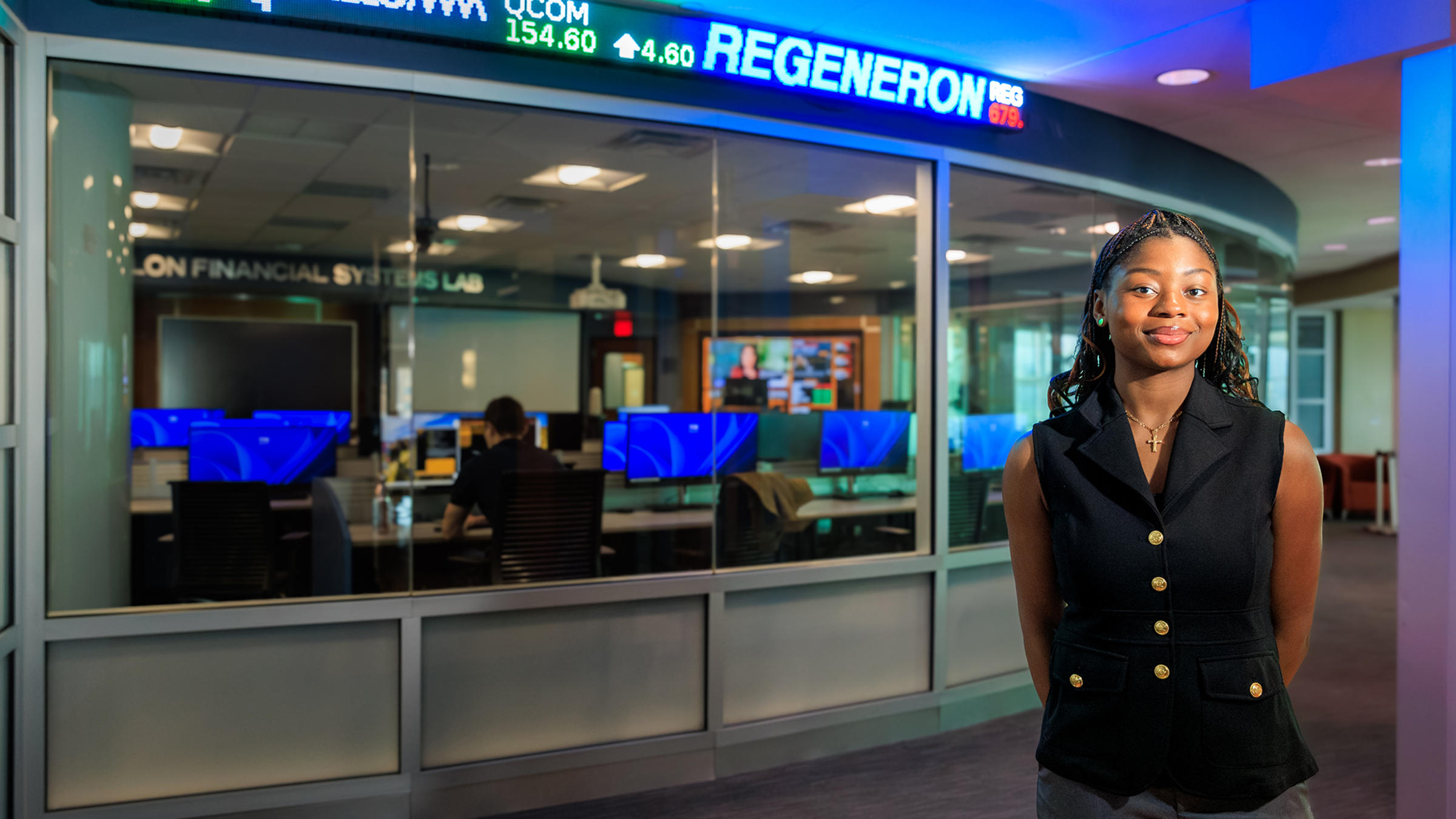 Victoria Okonkwo stands to the right of the stock exchange ticker outside the Hanlon Financial Systems Center