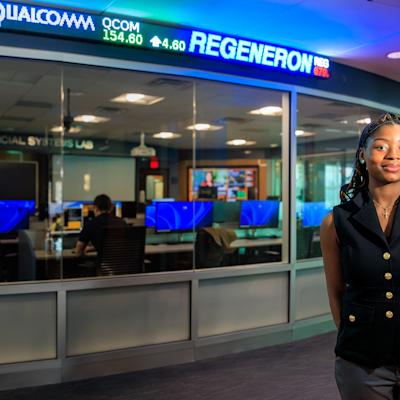 Victoria Okonkwo stands to the right of the stock exchange ticker outside the Hanlon Financial Systems Center