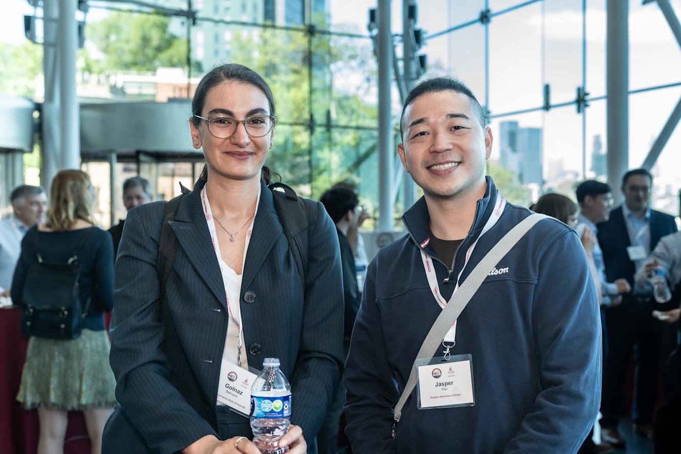 Two professional conference attendees pose together in a modern glass-walled venue.