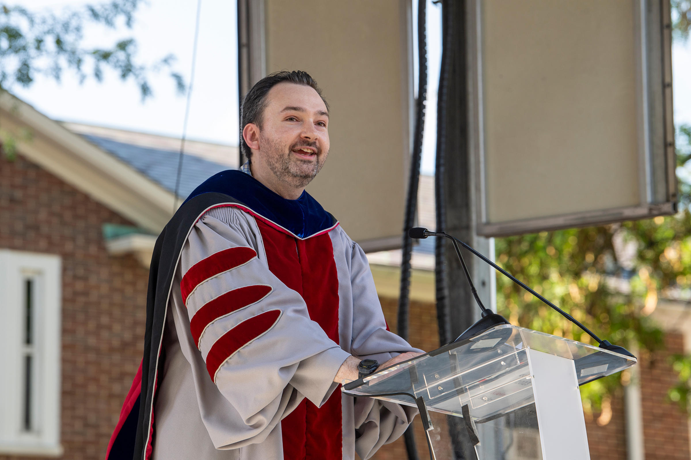Dr. Brendan Englot, Anson Wood Burchard Endowed Professor and Director of the Stevens Institute for Artificial Intelligence presents at podium in commencement attire