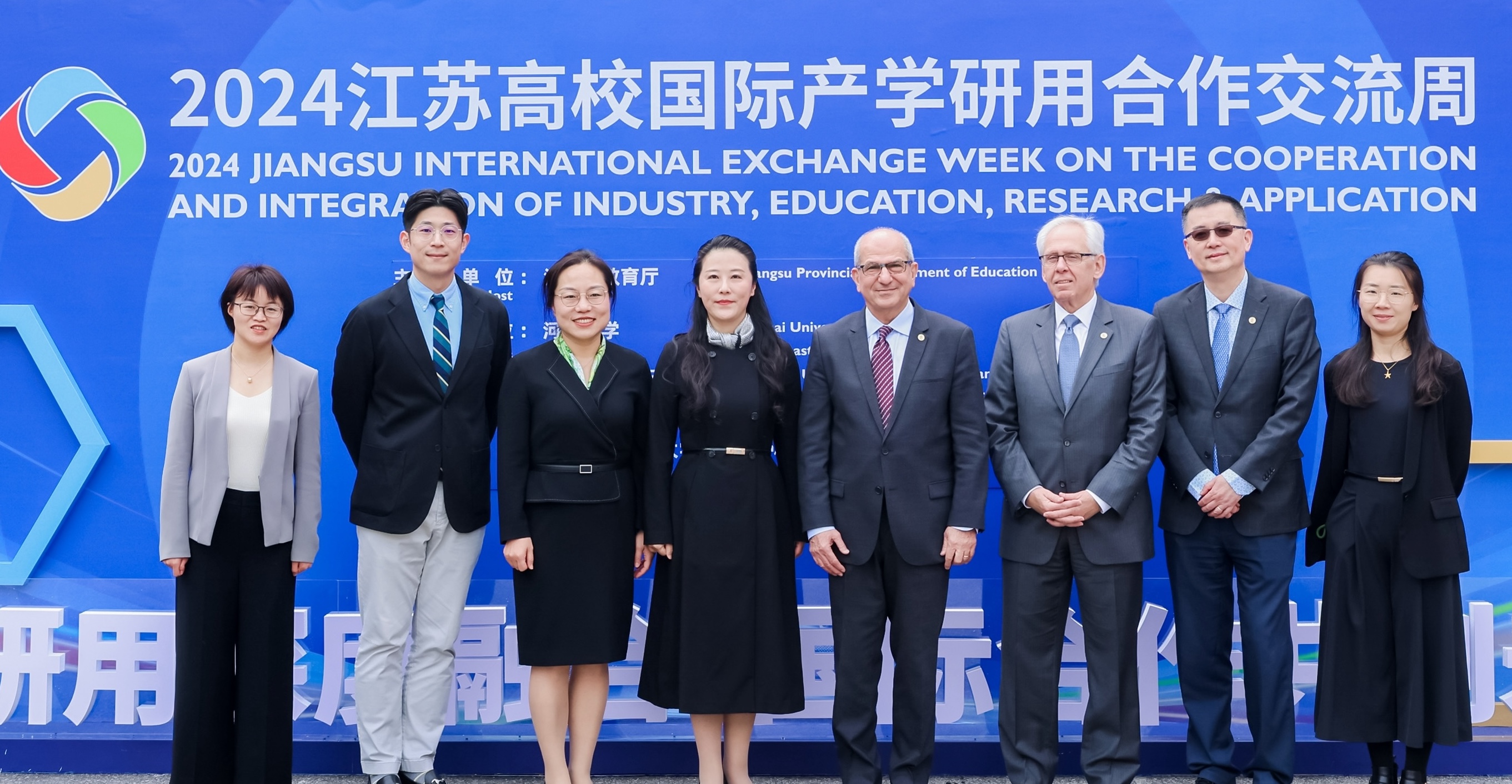 Stevens and Chinese-university officials standing in front of a sign at event in China