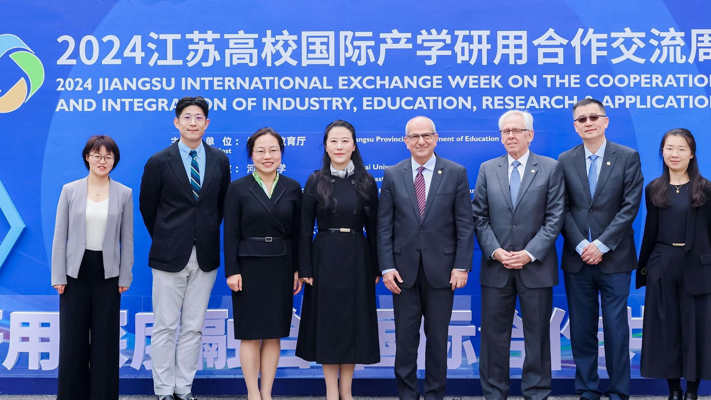 Stevens and Chinese-university officials standing in front of a sign at event in China