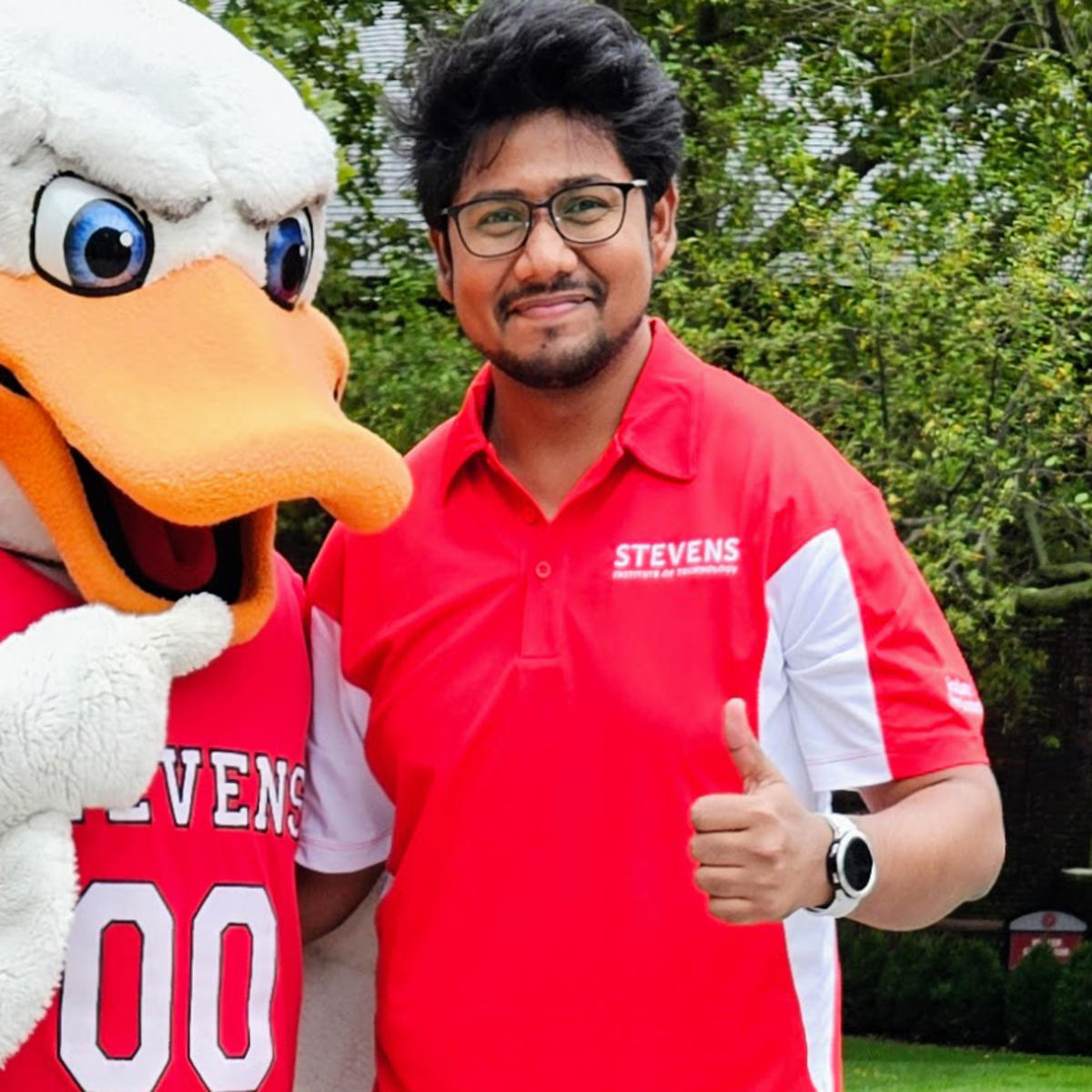 A man in a Stevens polo shirt poses next to Attila, Stevens' duck mascot, while the man in the polo shirt gives a thumbs up.