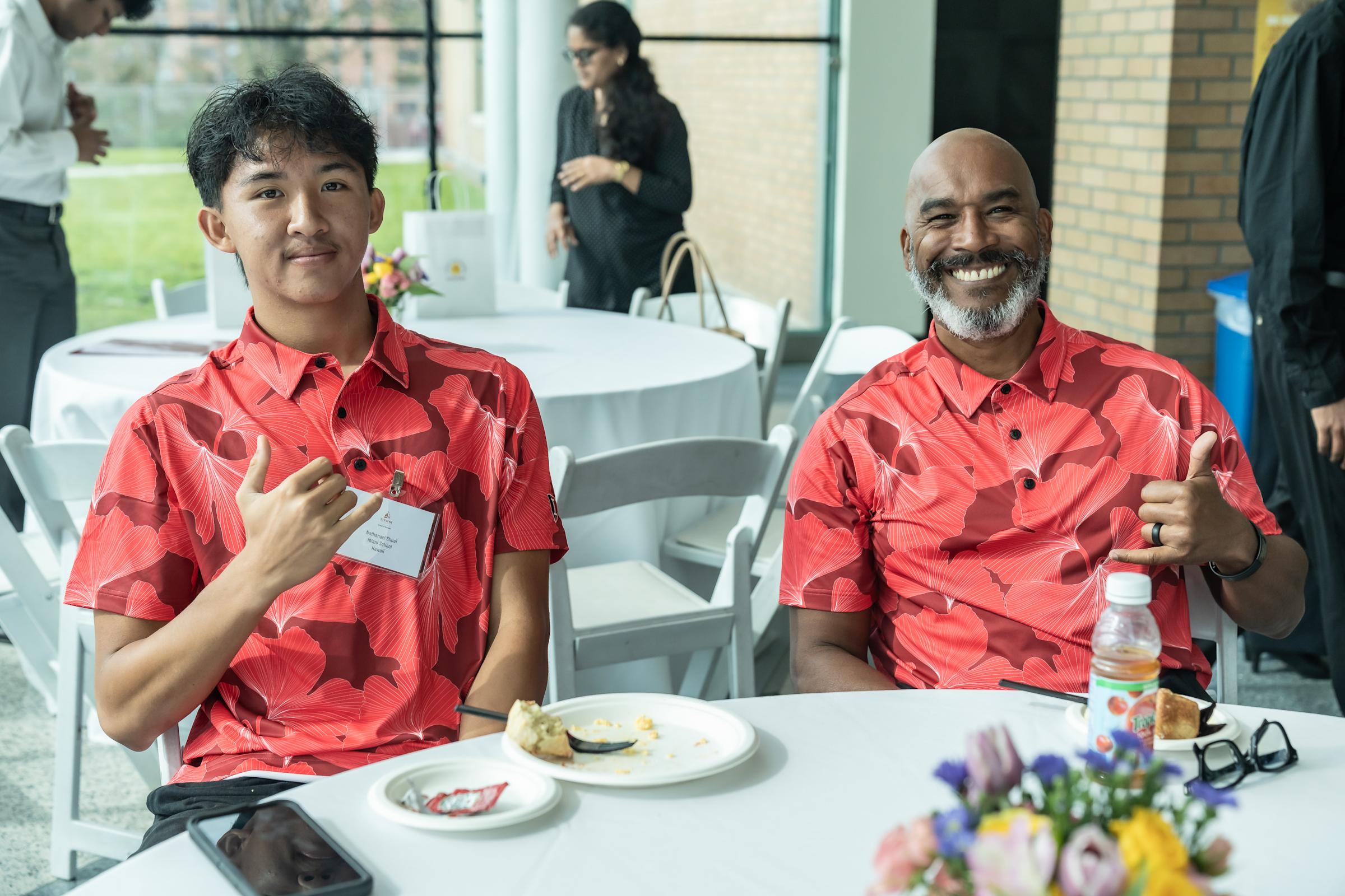 A student and teacher wearing Hawaiian shirts give the "shaka" sign. 