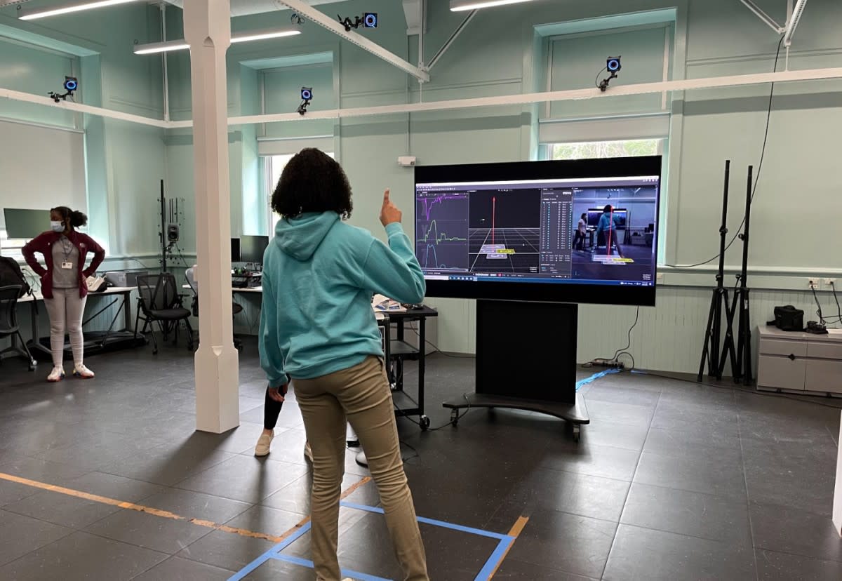 A high school girl stands in front of a computer screen watching her movements mirrored via sensors