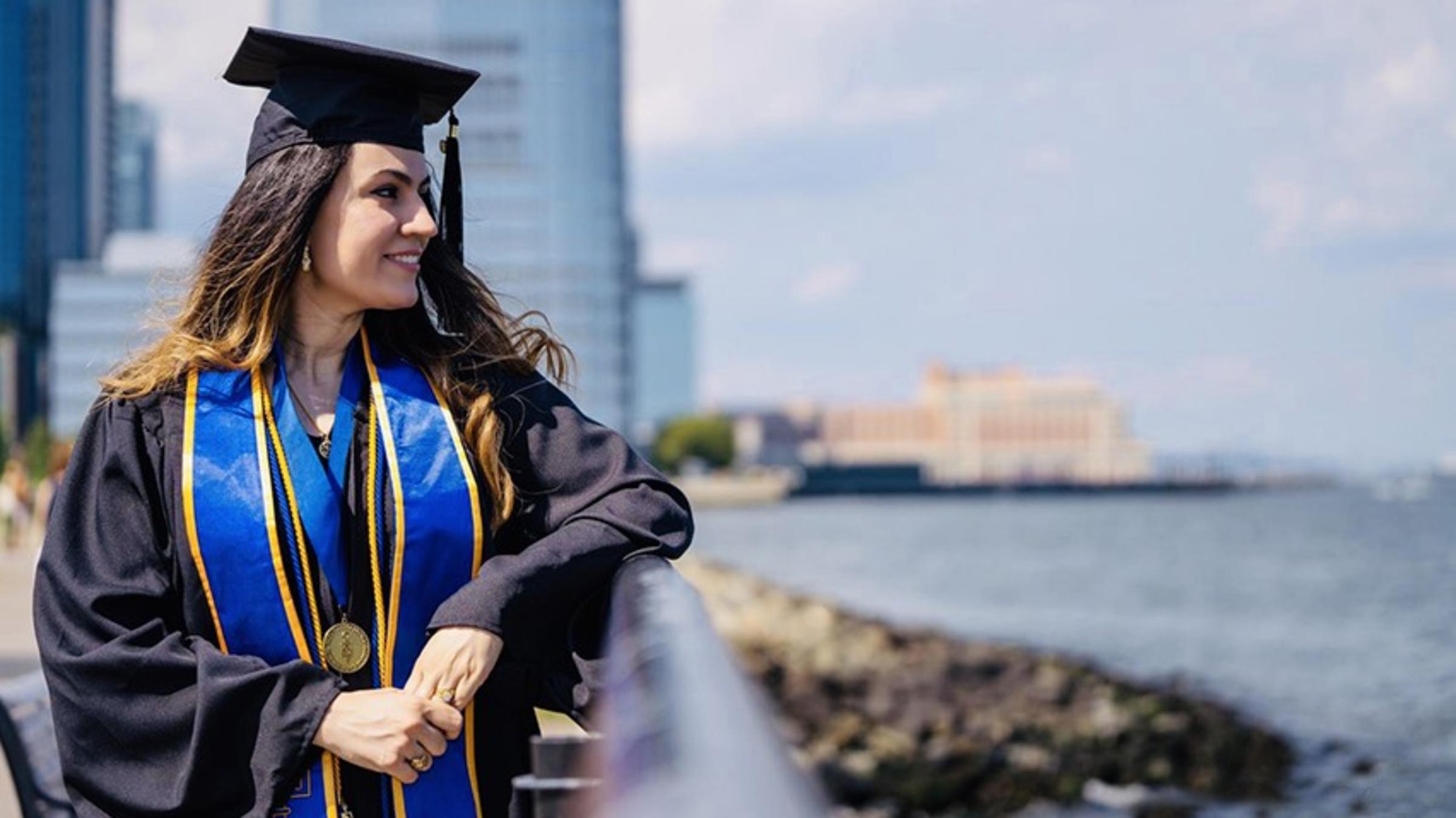 Fatine Zaaj along the Hudson River, dressed in her cap and gown.