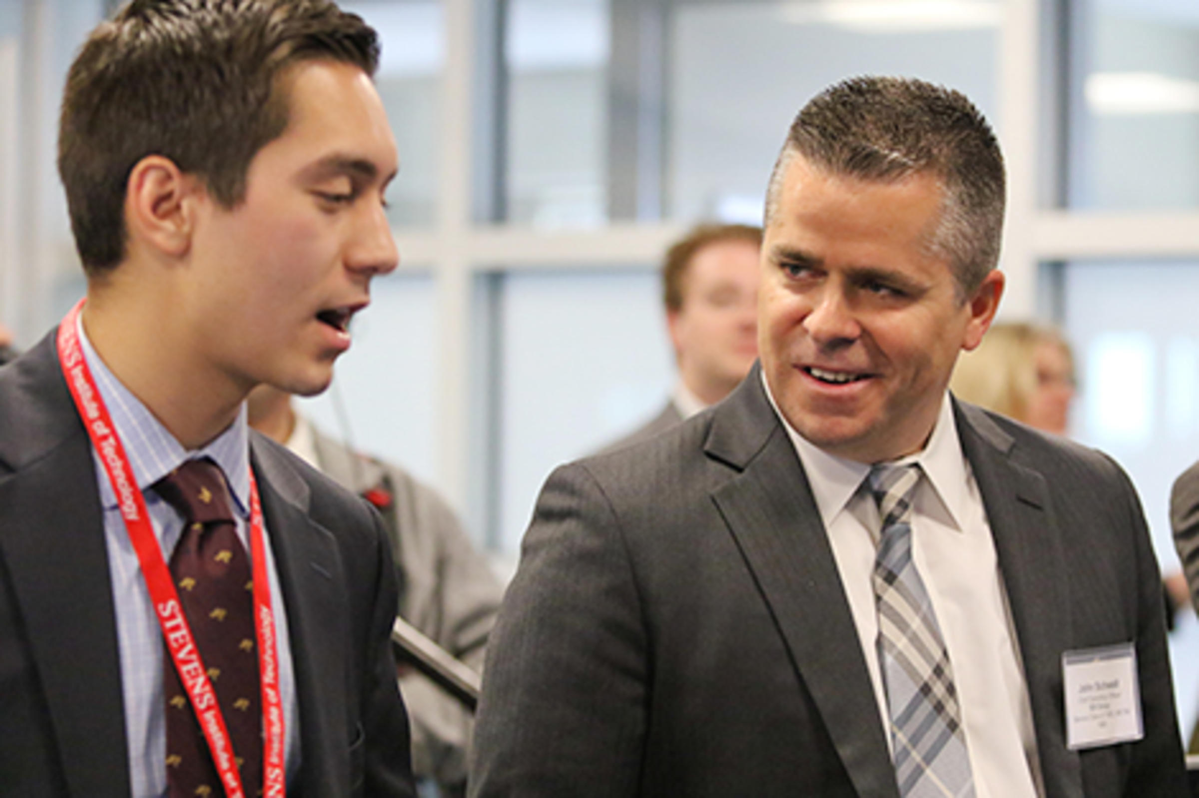 John Schwall, in a dark suit, talks to a male student in the Hanlon Lan at Stevens.