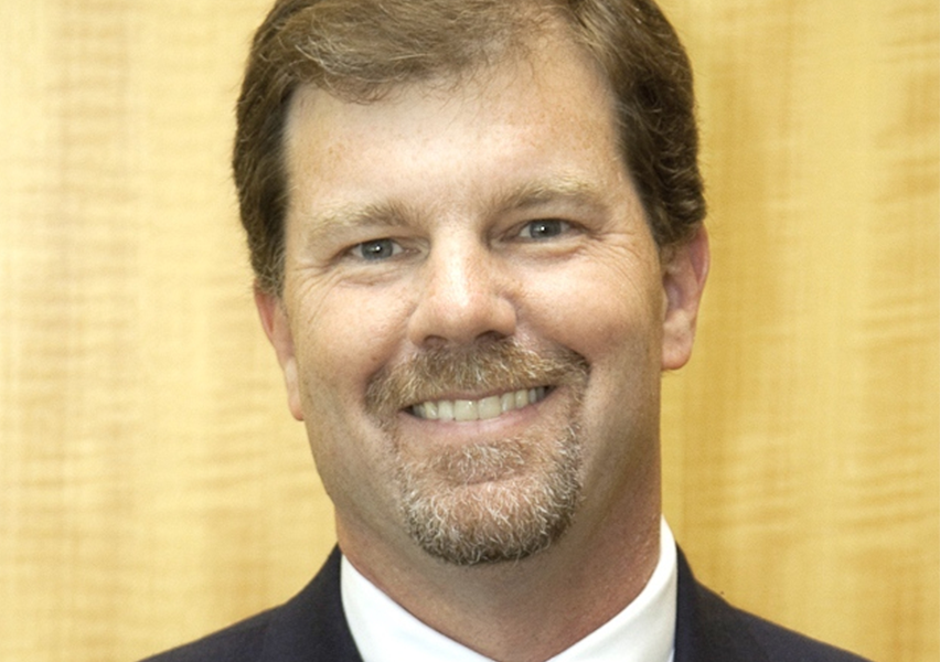 Close up headshot of Thomas A. McDermott Jr., Deputy Director of SERC at Stevens, wearing a black suit, white collared shirt, and blue tie. 