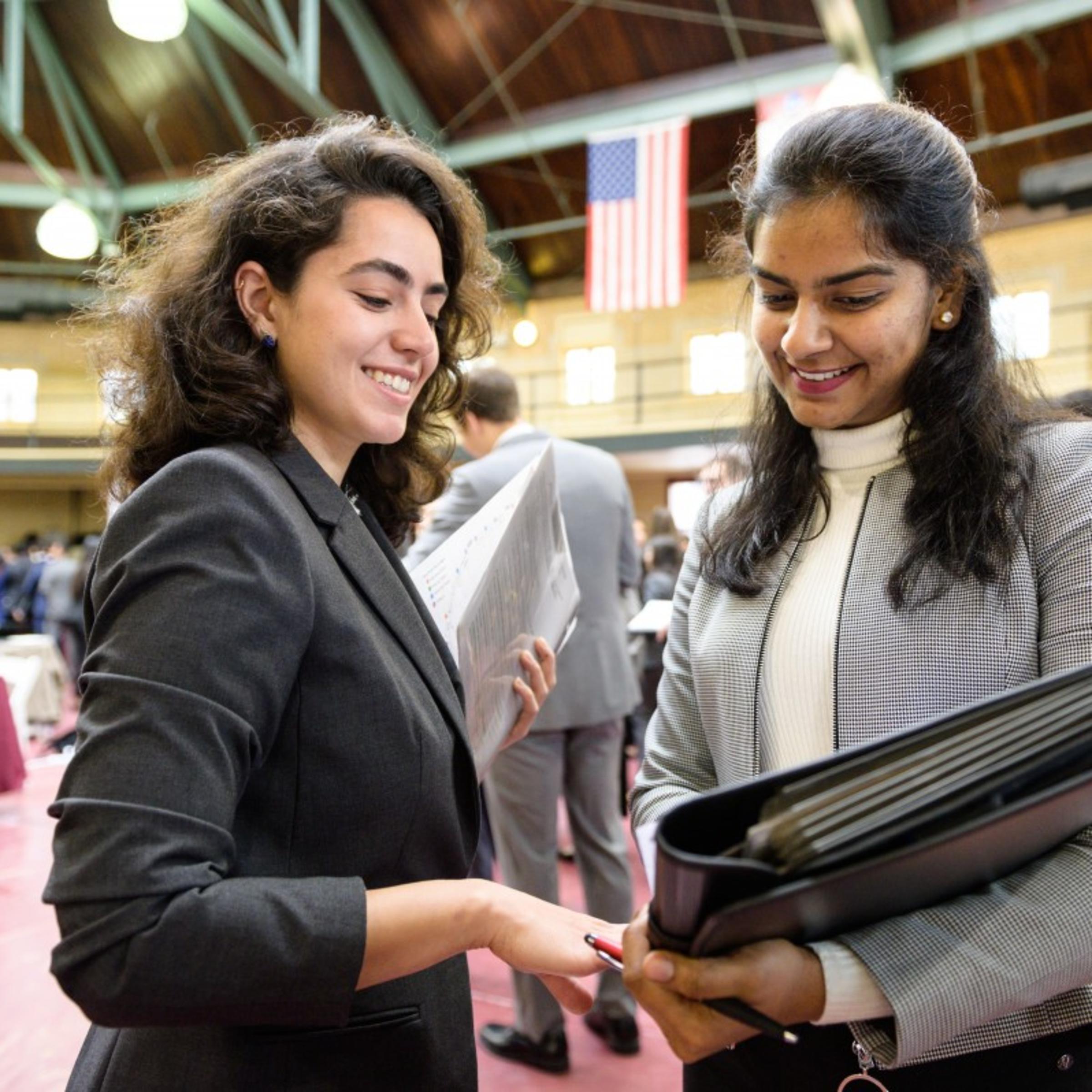 A female recruiter (left) at the internship fair chats with a female student as they go over her resume
