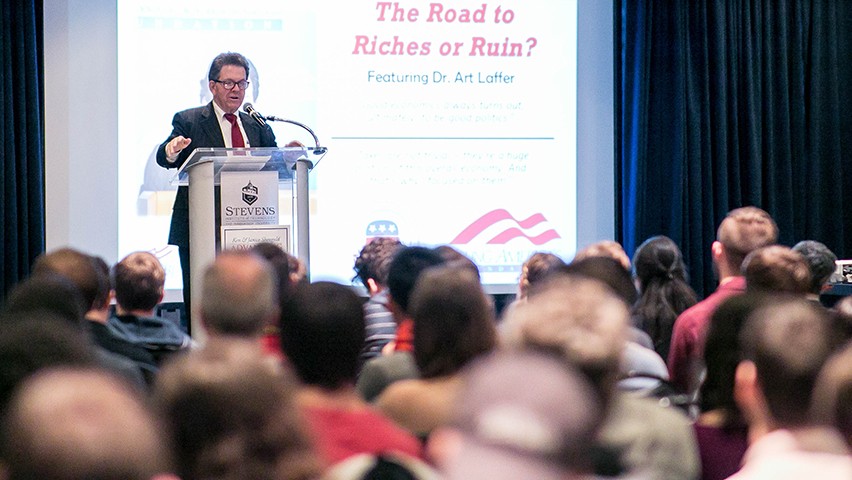 Dr. Art Laffer at a podium before a crowd of Stevens students.