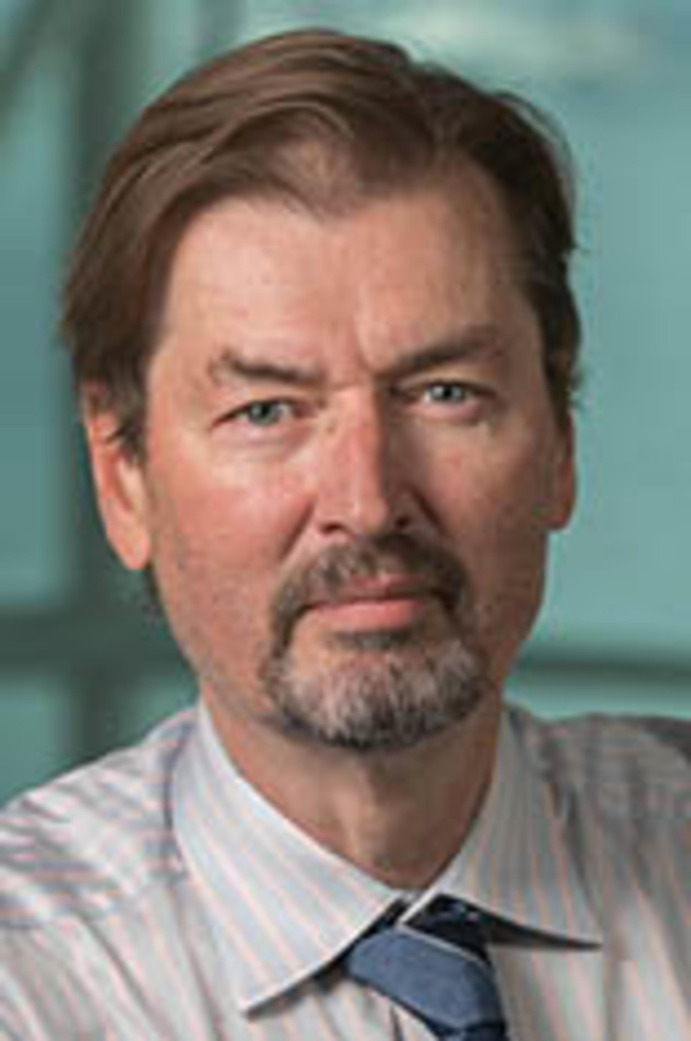 Headshot of Dr. George Calhoun in a striped shirt with the New York City skyline in the background.