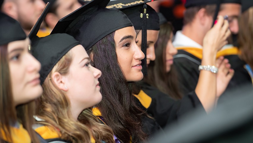 A group of female business students watching the presentation of diplomas at commencement.