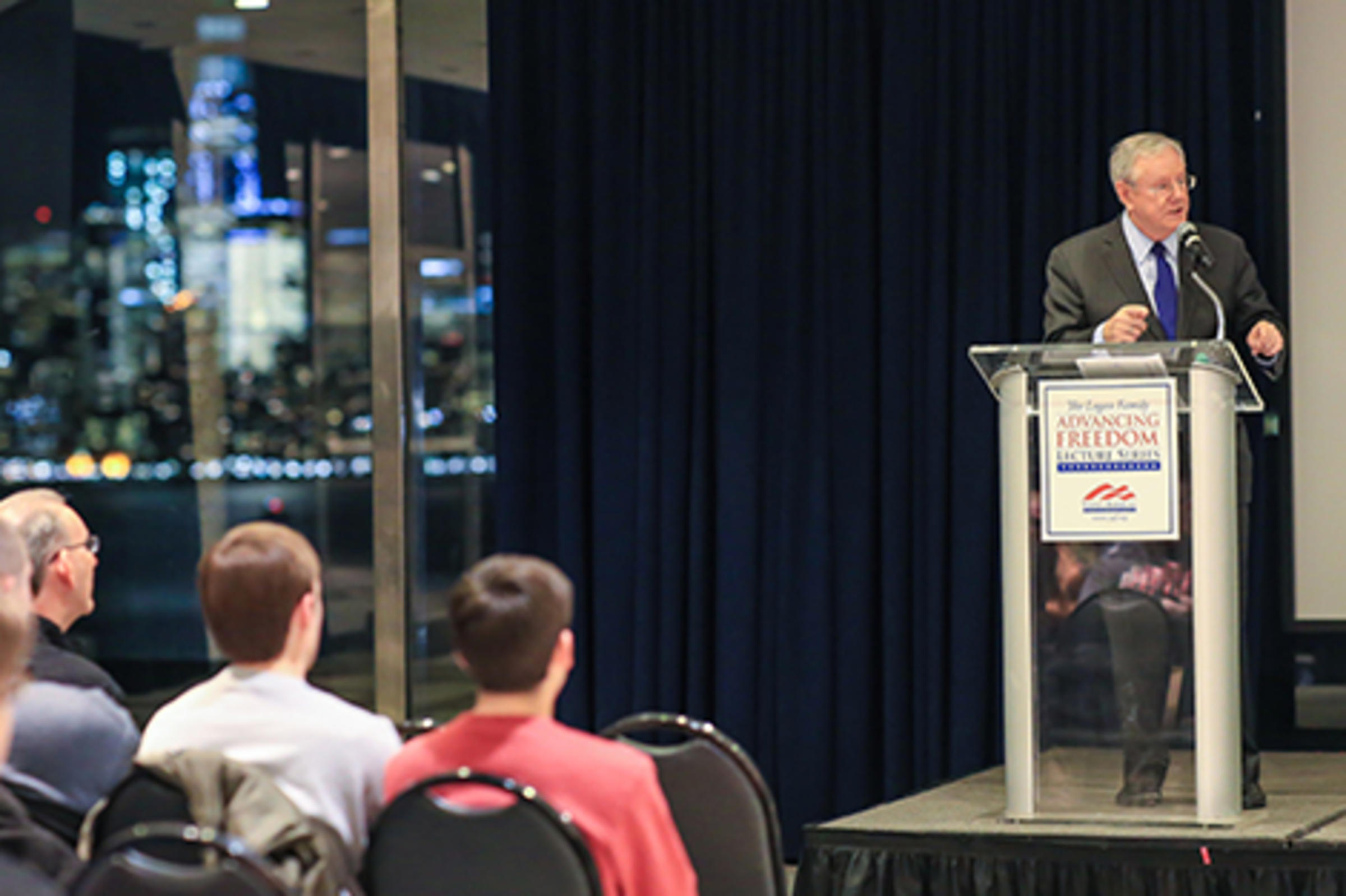 Steve Forbes speaks to the audience. The New York skyline can be seen in the background.