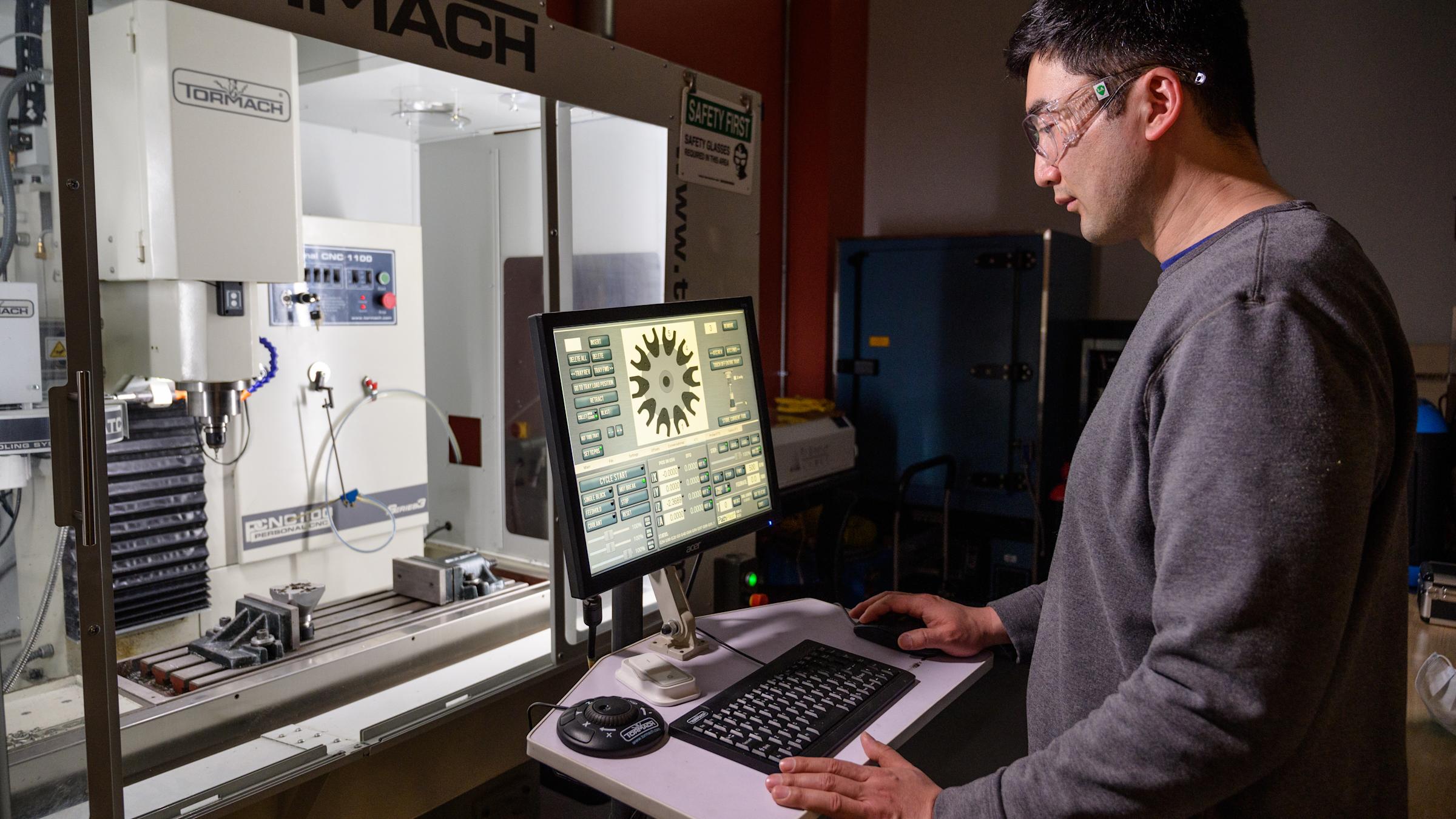 Male student with a grey shirt and glasses working on a computer with an experiment in front of him.