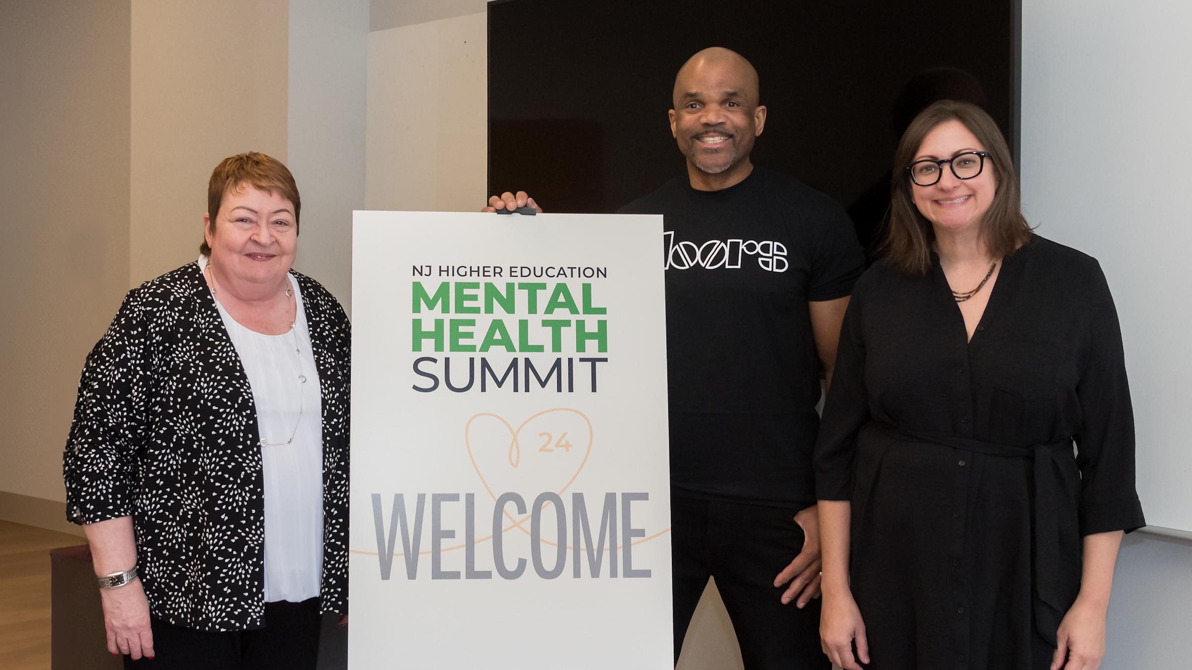 Three people posed in front of the Mental Health Summit sign