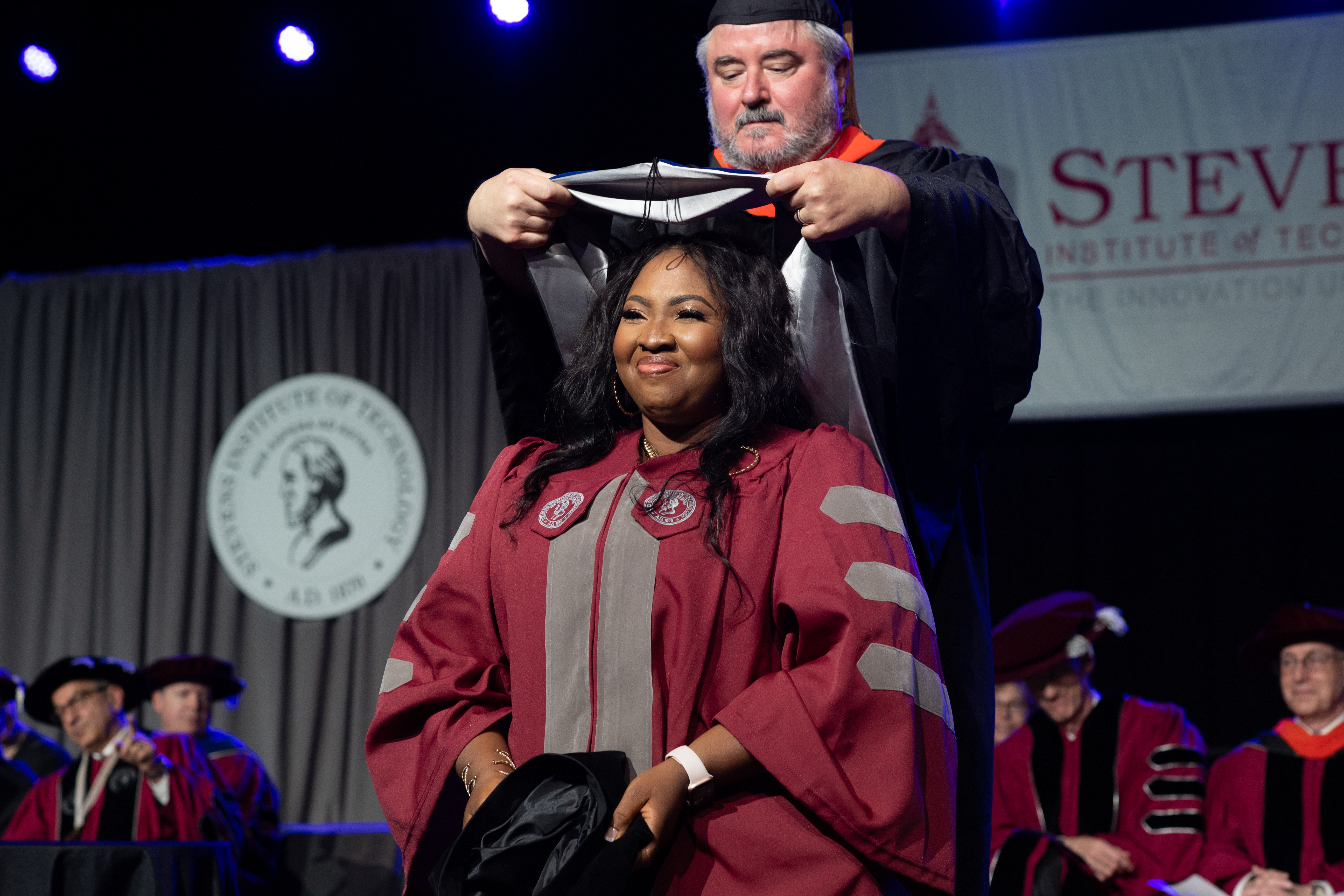A Ph.D. graduate is hooded by her advisor at commencement.