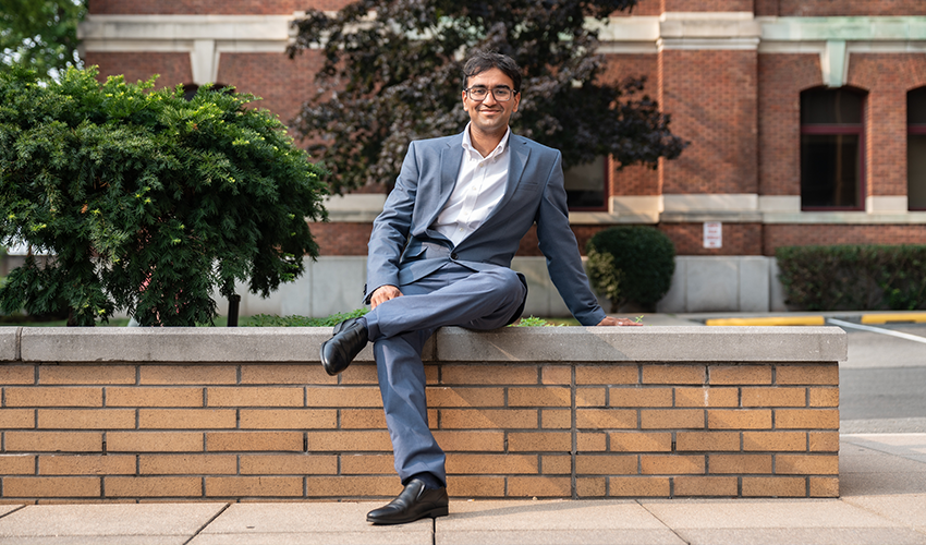 Darsh sits in a blue suit on a ledge in front of Babbio 