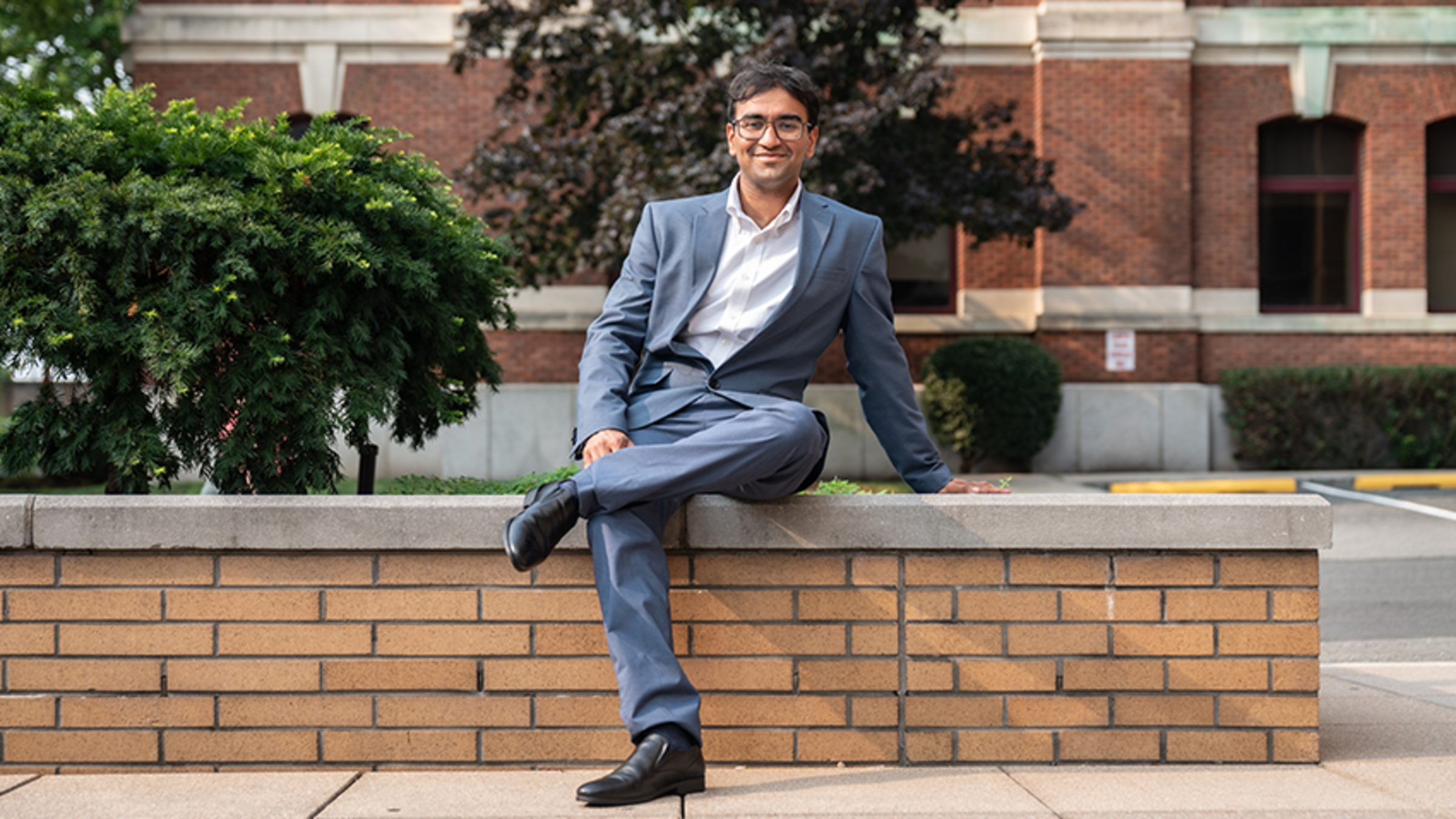 Darsh sits in a blue suit on a ledge in front of Babbio