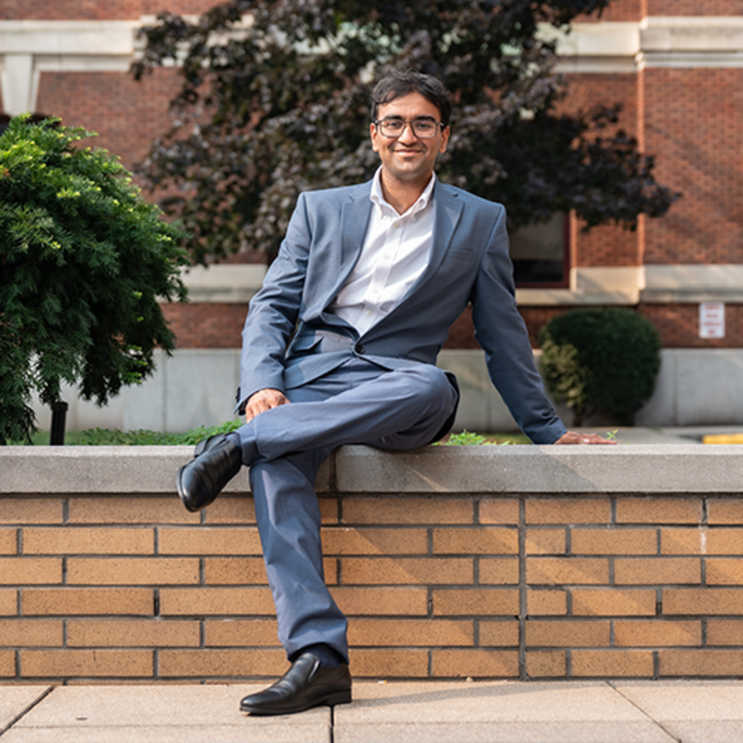 Darsh sits in a blue suit on a ledge in front of Babbio