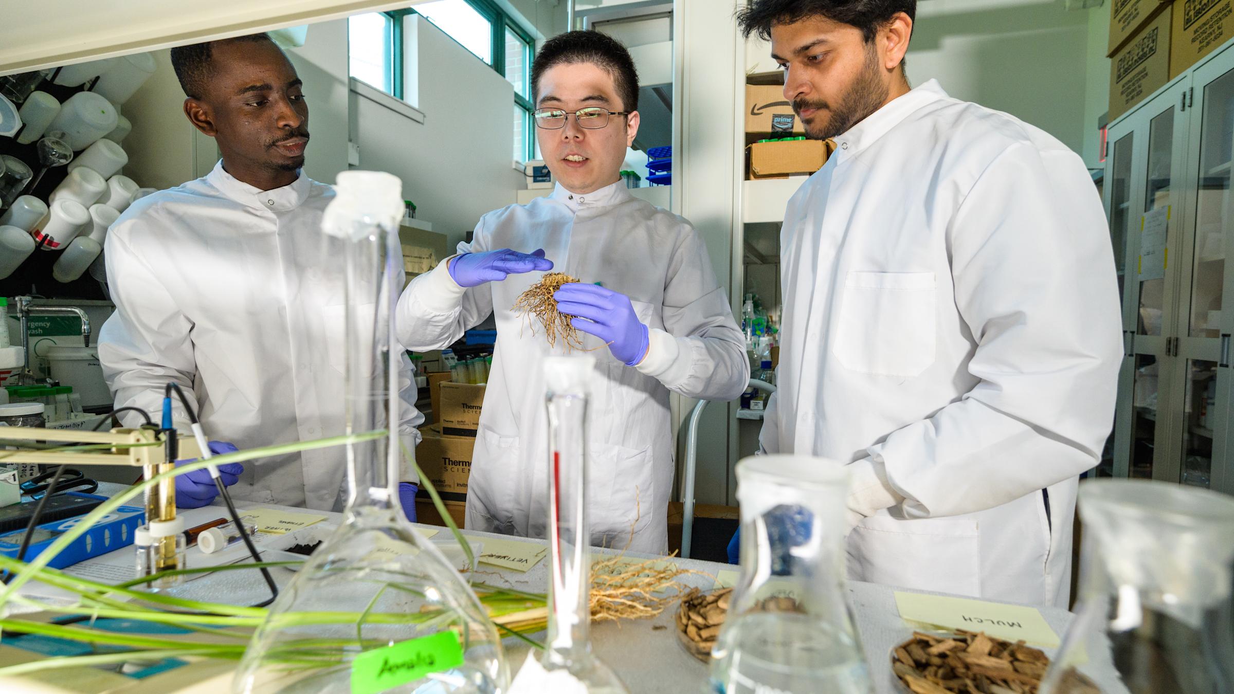 Three male students in lab gear running an experiment