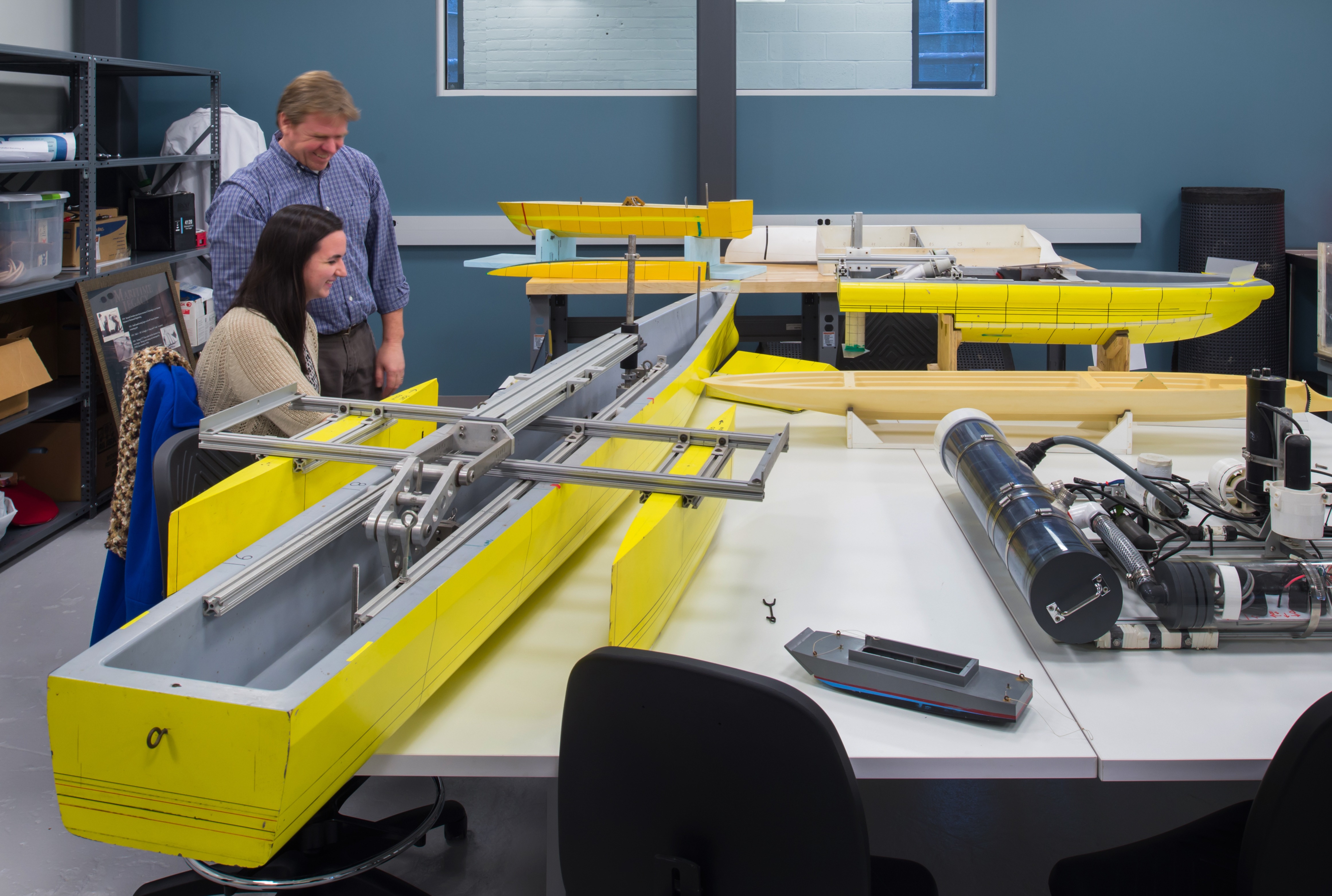 An instructor working with a student on building a water vessel shaped like a canoe in a shop.