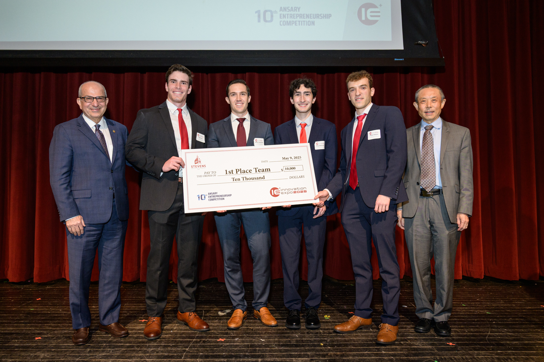A group of students poses with Stevens's administrators while holding a large check for $10,000.