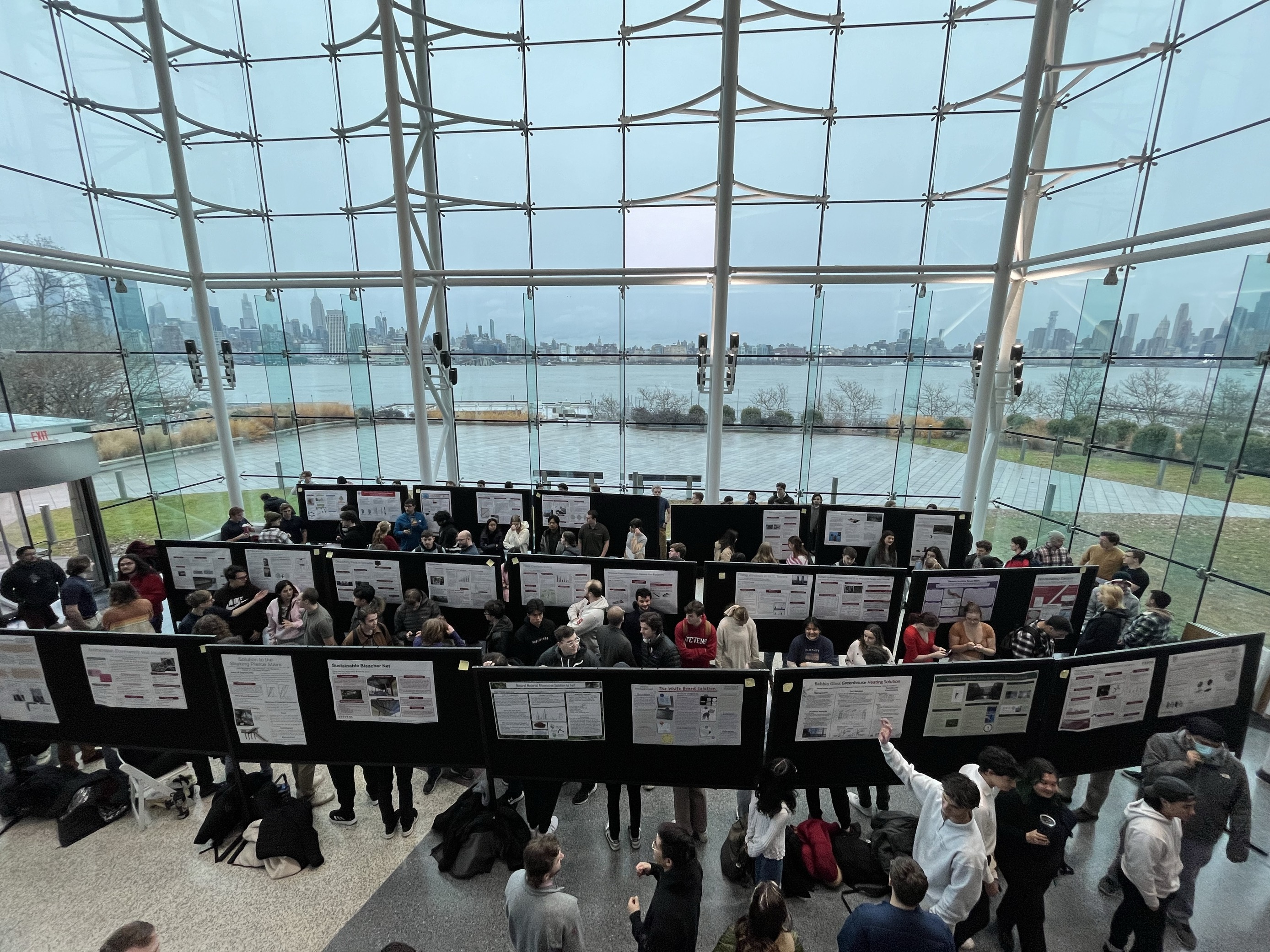 Students in a glass atrium area look at poster presentations.