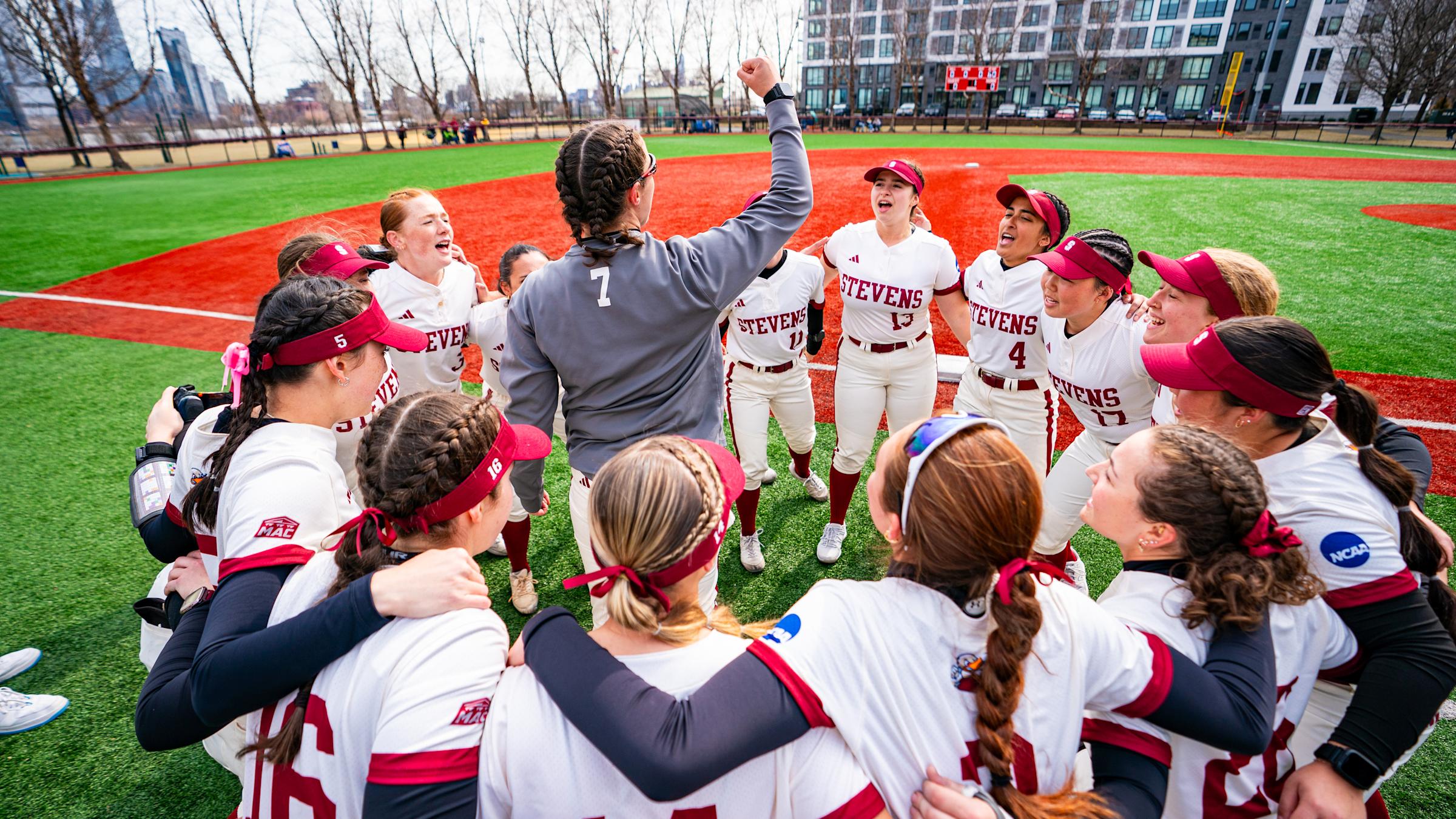 Stevens softball players gather in a huddle on the field together