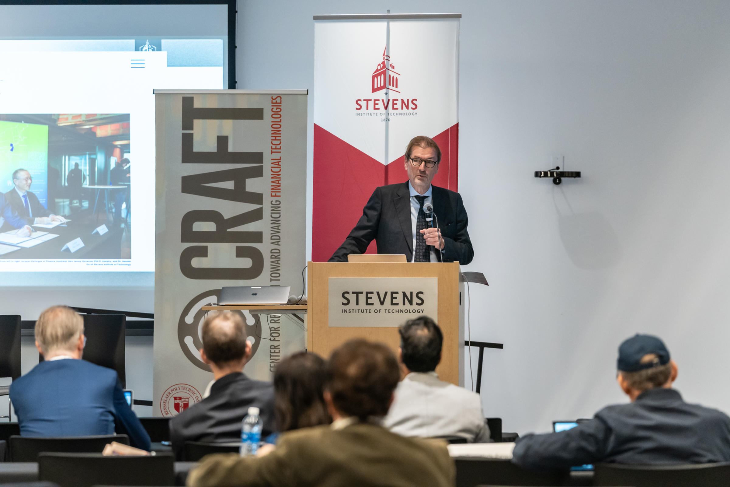 George Calhoun holds a microphone and addresses the crowd from behind a podium.