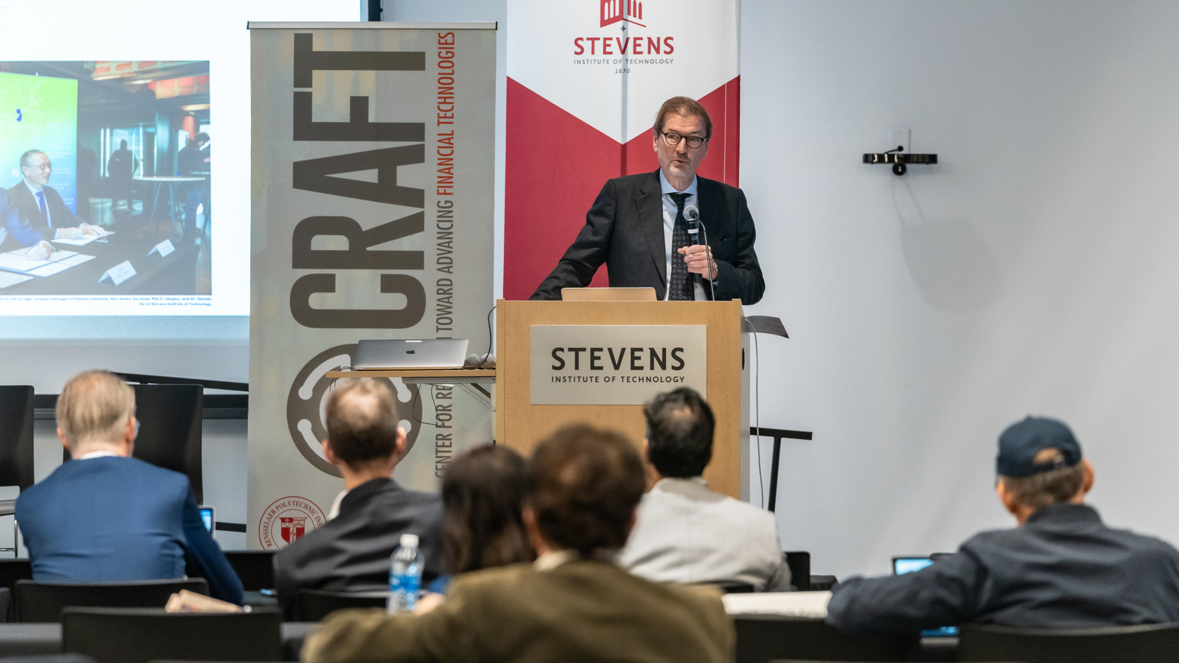 George Calhoun holds a microphone and addresses the crowd from behind a podium.