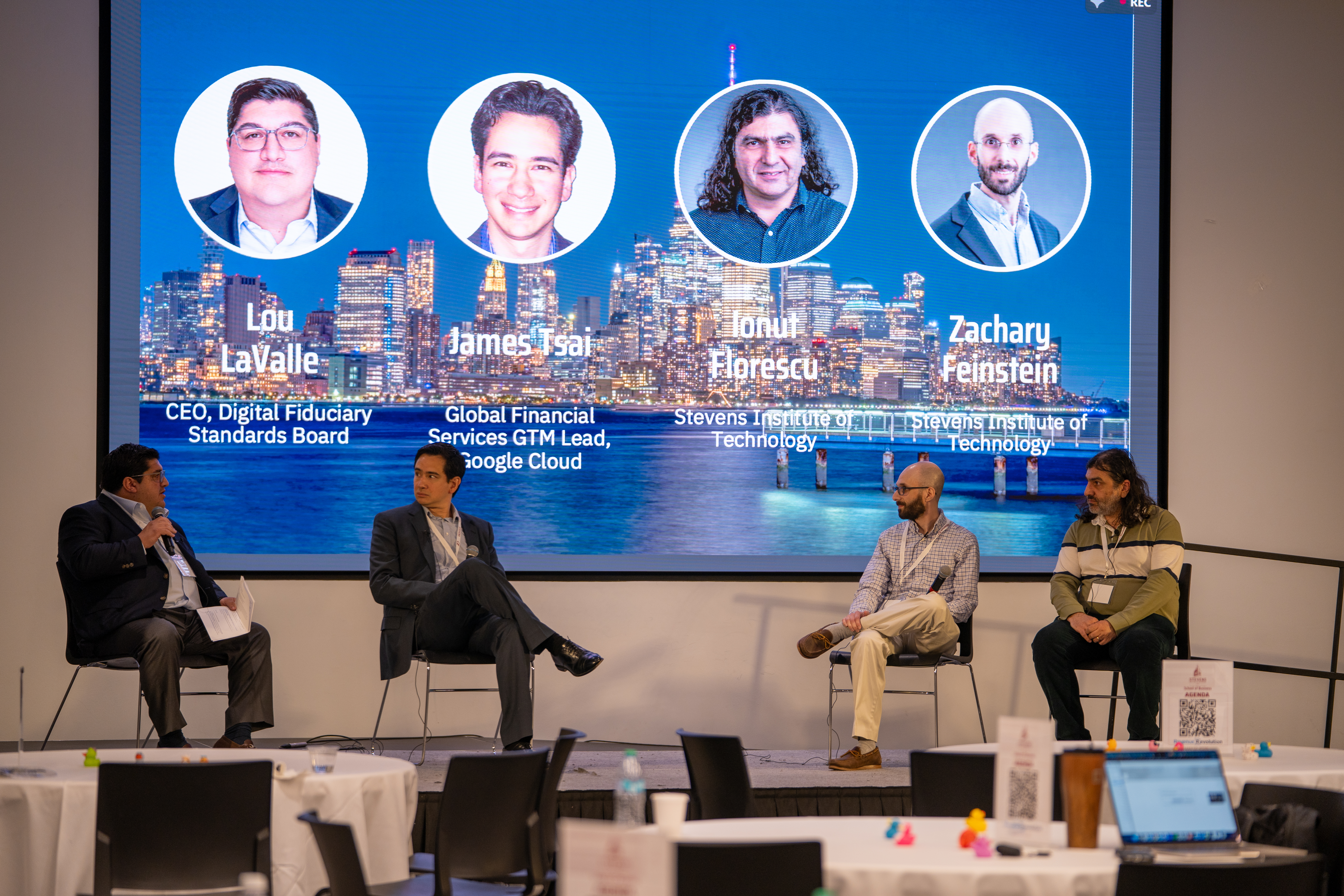 our panelists sit on stage beneath large screen showing headshots and credentials: Lou LaValle (CEO, Digital Fiduciary Standards Board), James Tsai (Google Cloud GTM Lead), Ionut Elprescu (Stevens), and Zacharu Feinstein (Stevens). 