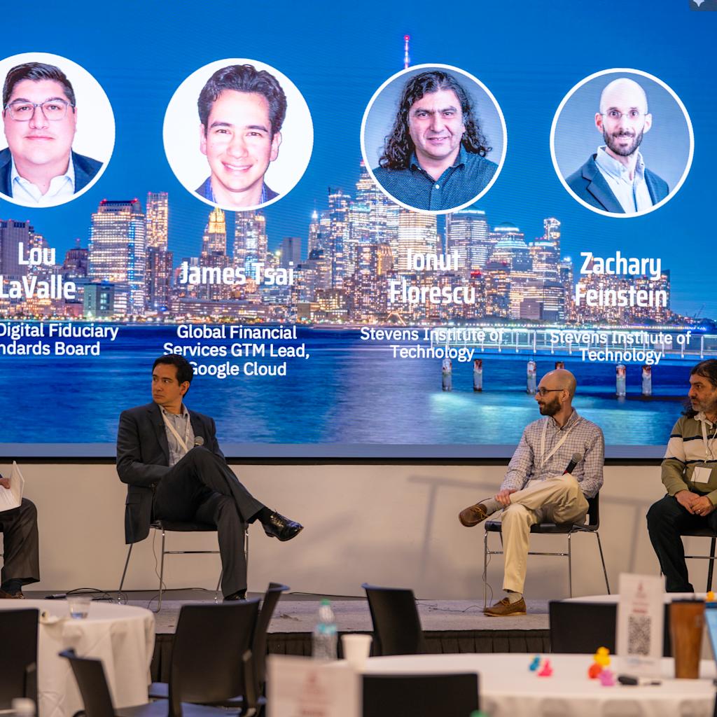 our panelists sit on stage beneath large screen showing headshots and credentials: Lou LaValle (CEO, Digital Fiduciary Standards Board), James Tsai (Google Cloud GTM Lead), Ionut Elprescu (Stevens), and Zacharu Feinstein (Stevens).