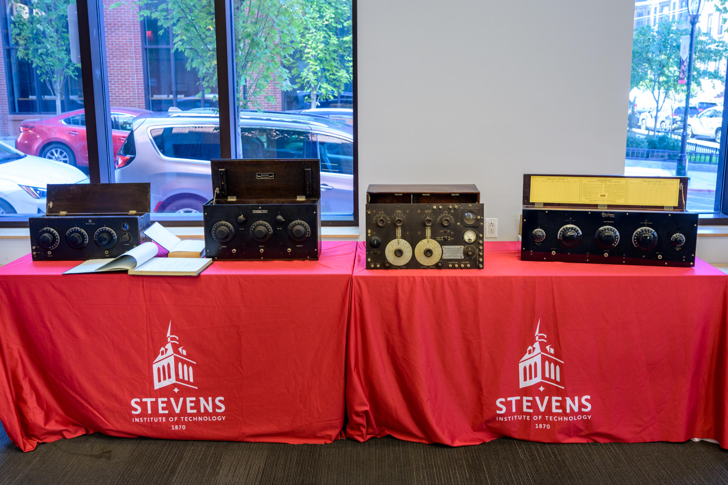 Four antique radios on two tables covered in Stevens-branded tablecloths.
