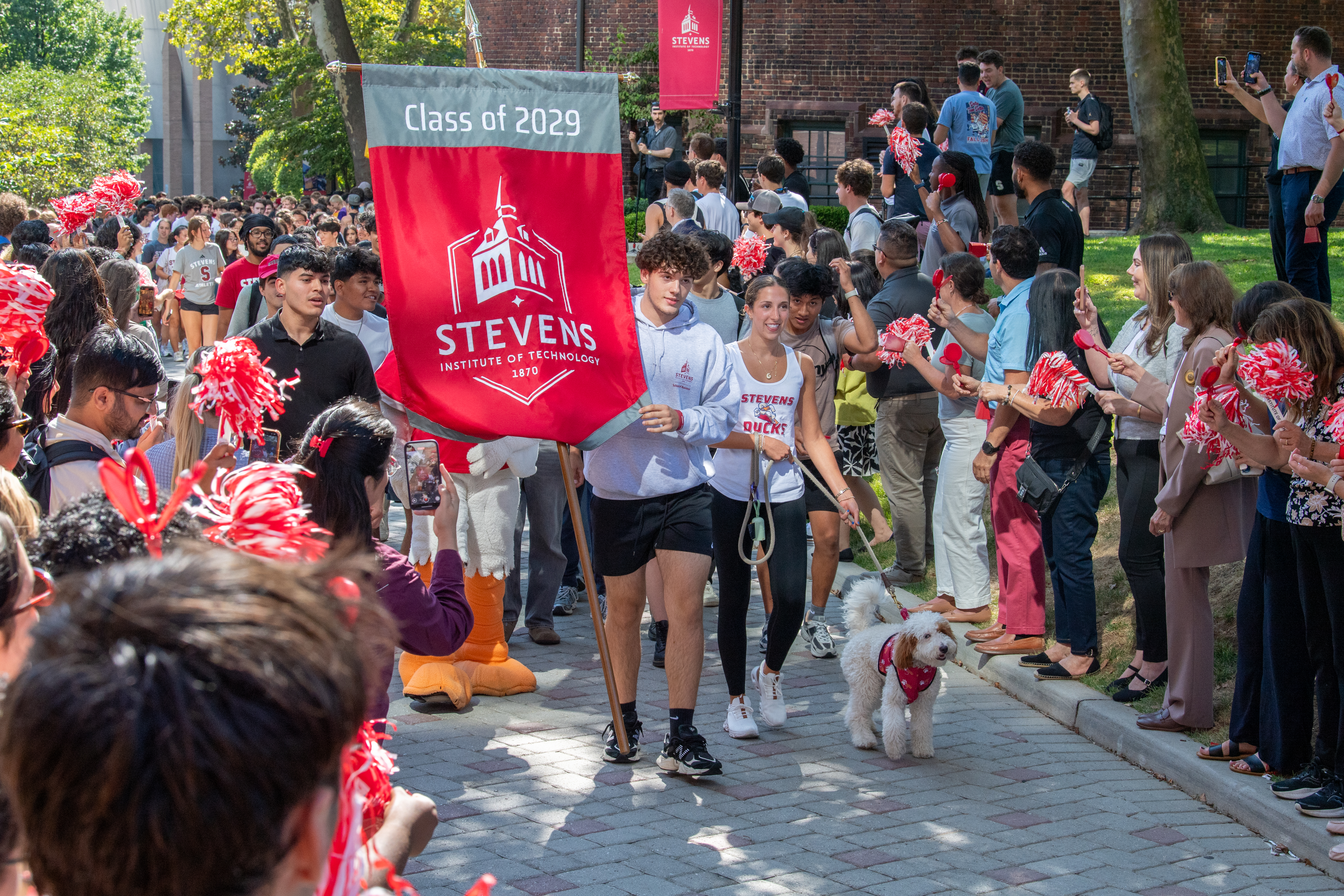 A man carries a "Class of 2029" flag in front of a group of people.