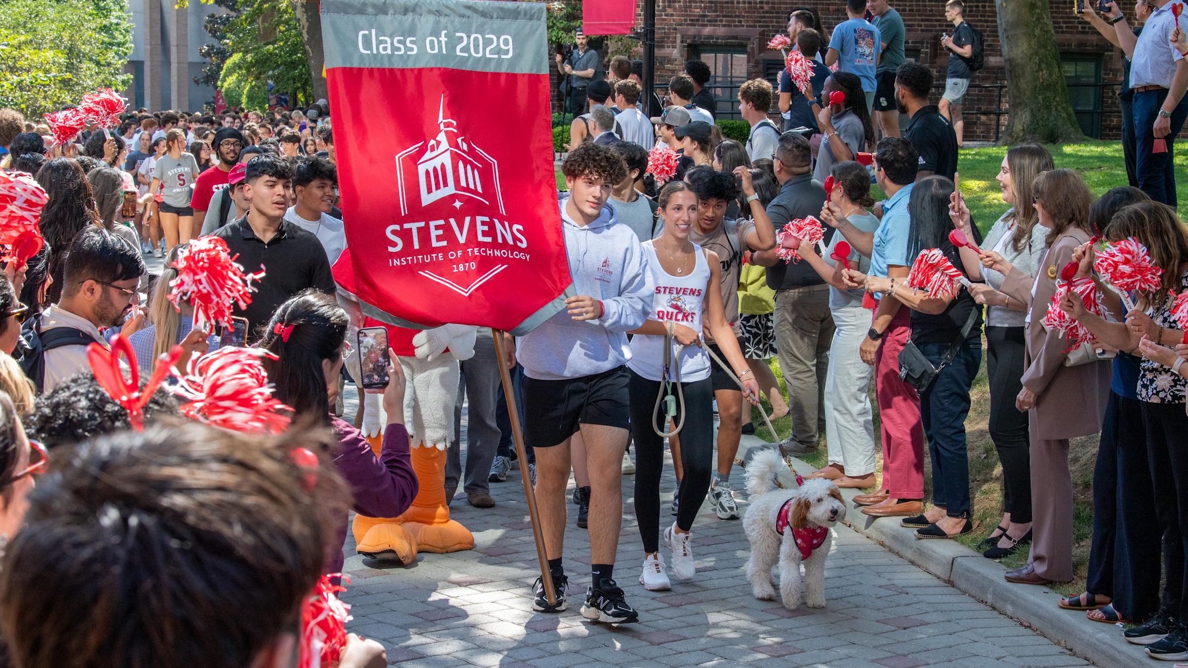 A man carries a "Class of 2029" flag in front of a group of people.