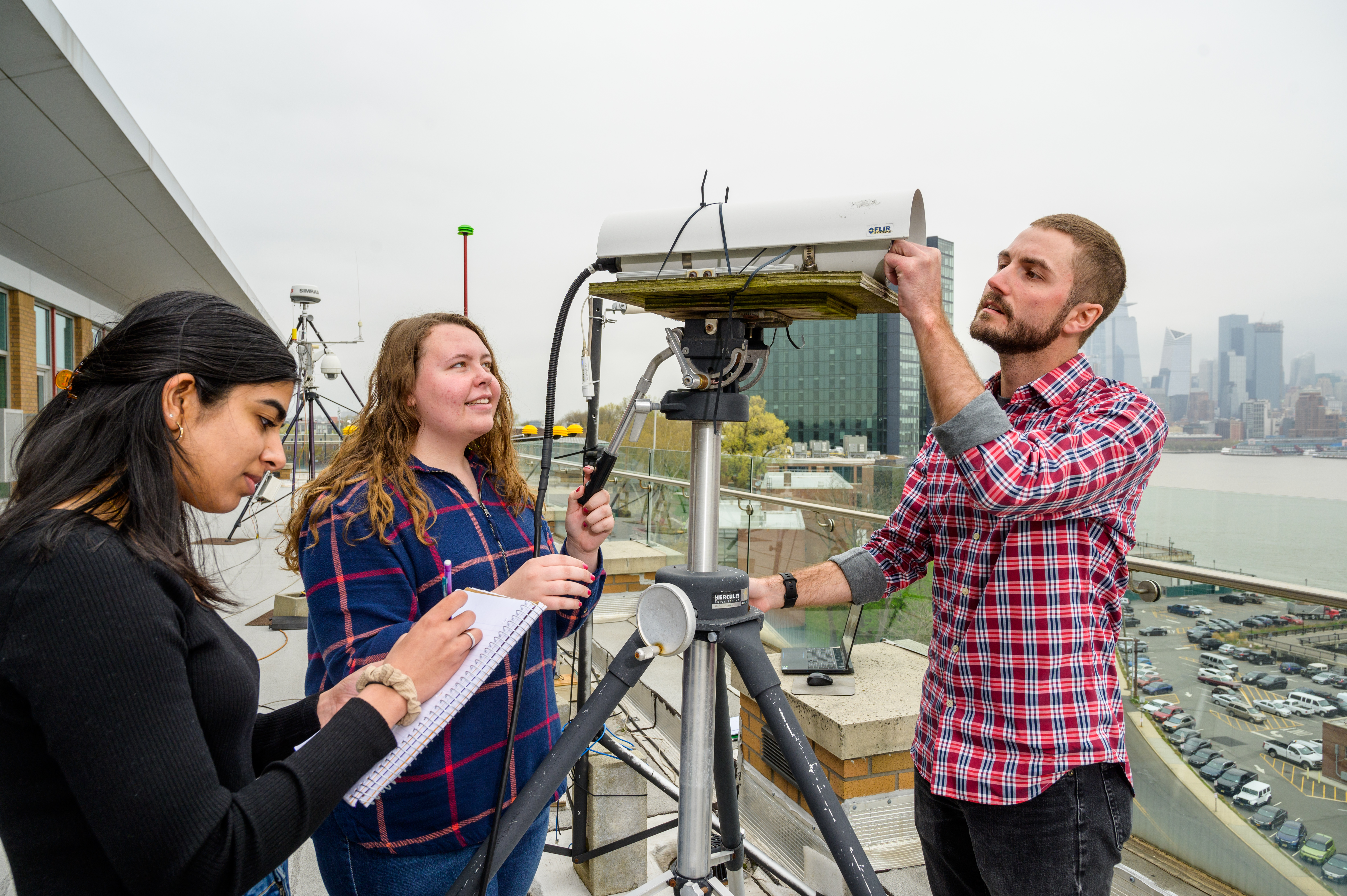 Students on a roof work with a monitoring device.