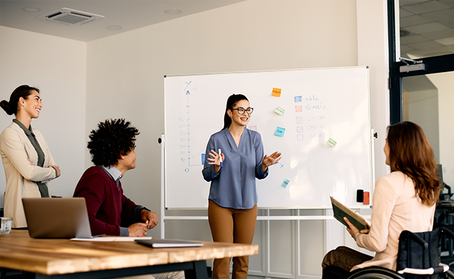 Happy entrepreneur talking to her coworkers about inclusive business strategy while holding presentation in the office.