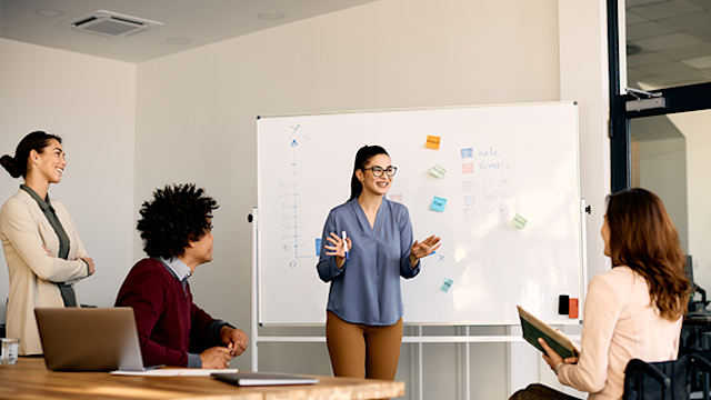 Happy entrepreneur talking to her coworkers about inclusive business strategy while holding presentation in the office.